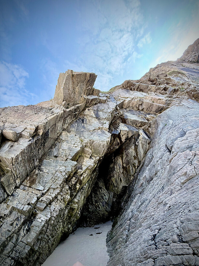 Rocky cave opening on a beach, with light clouded sky