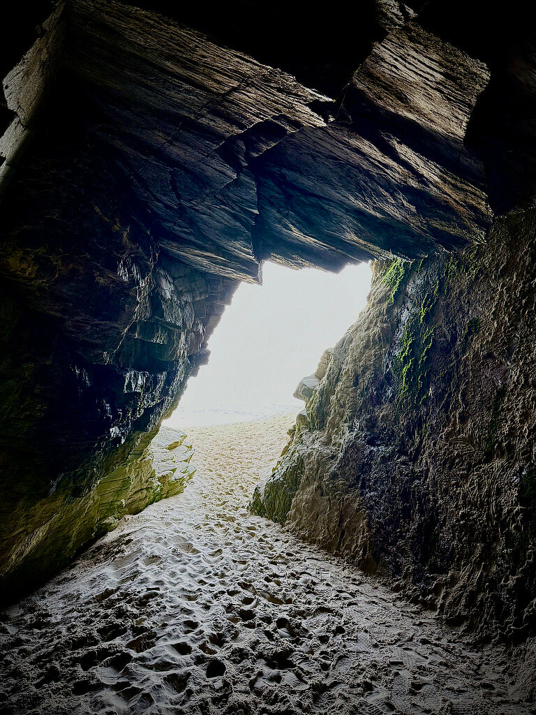 View from inside a beach cave looking out at the bright sun. 
