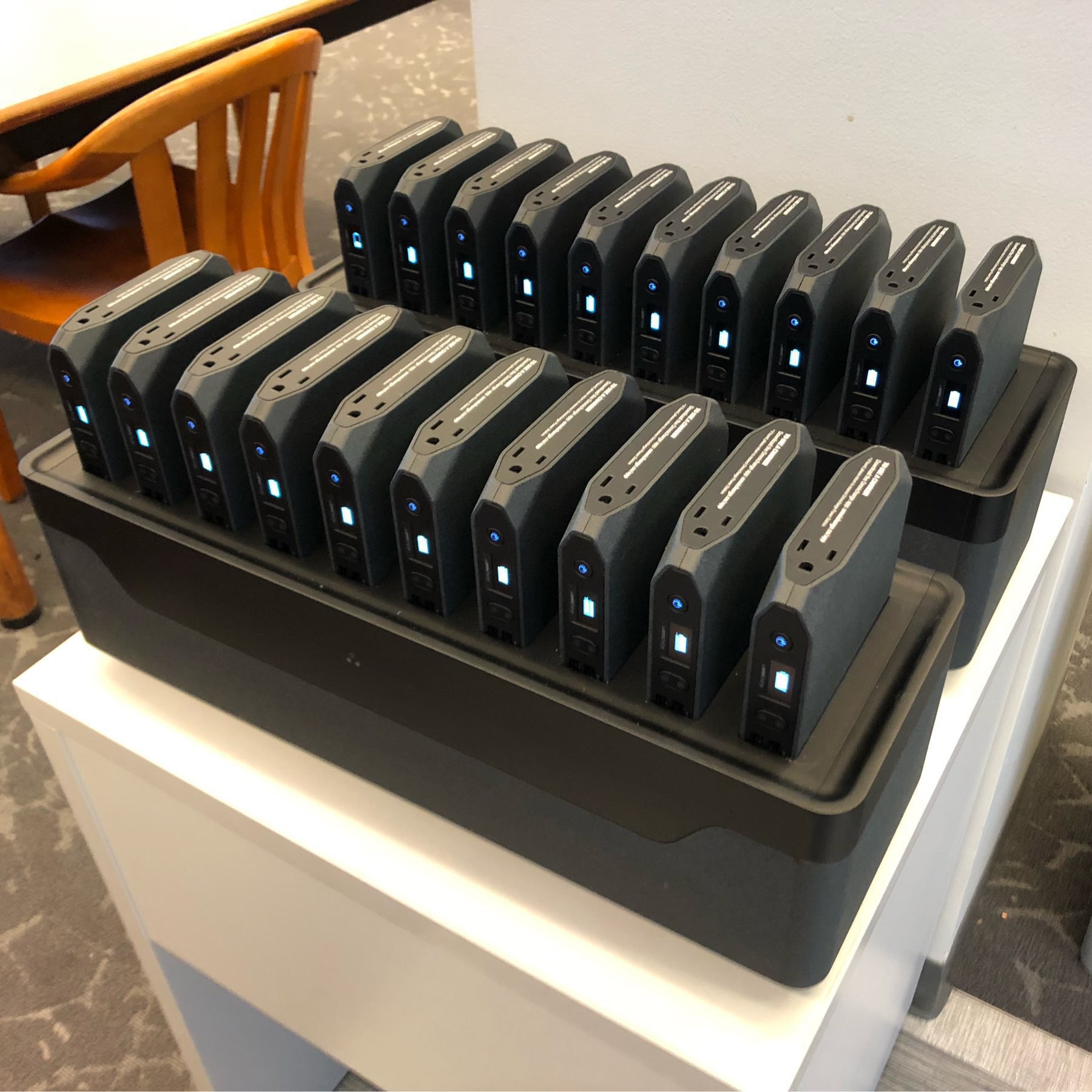 Two rows of black portable laptop chargers with white lights on them. 