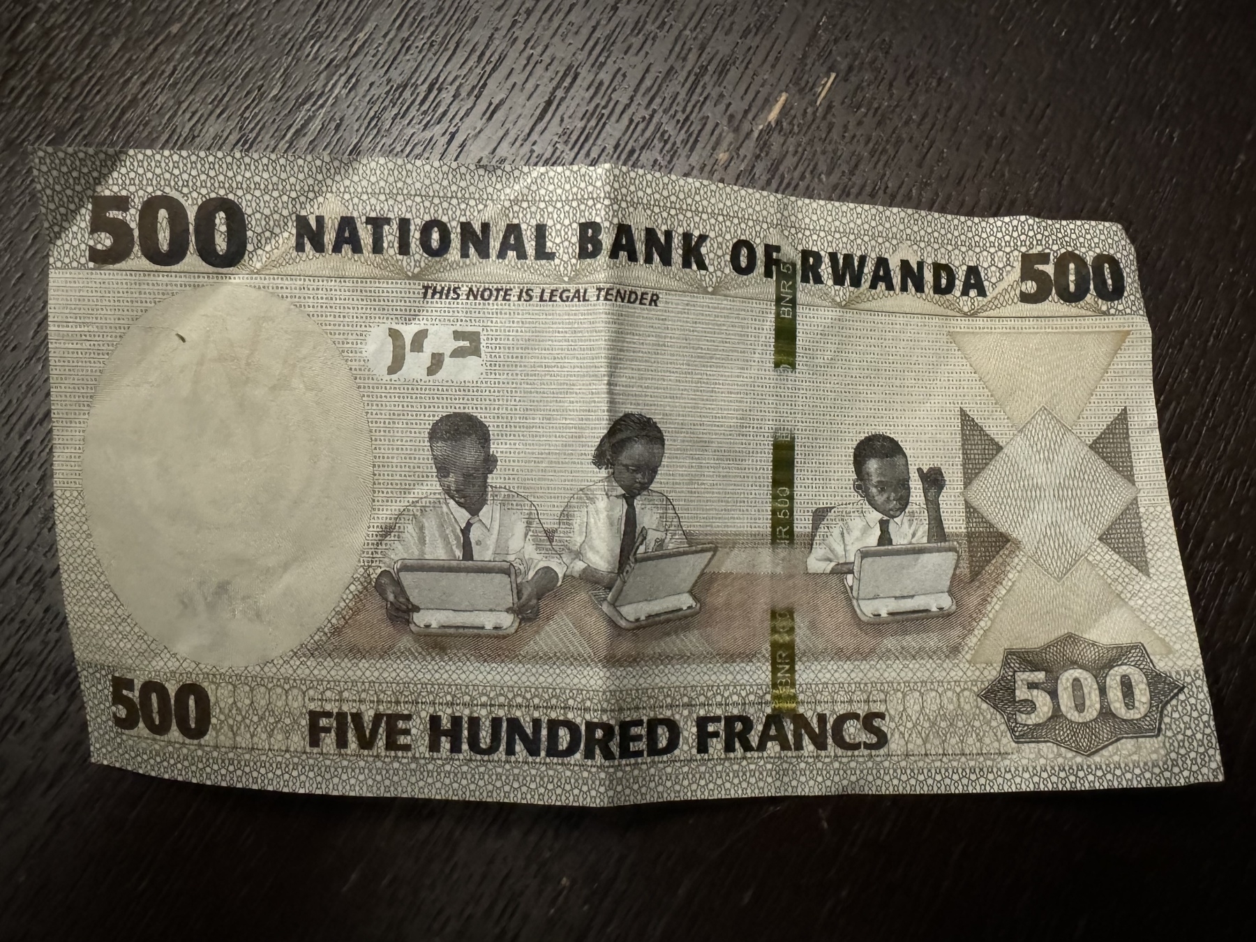 A bank note shows three children typing on small laptops. 