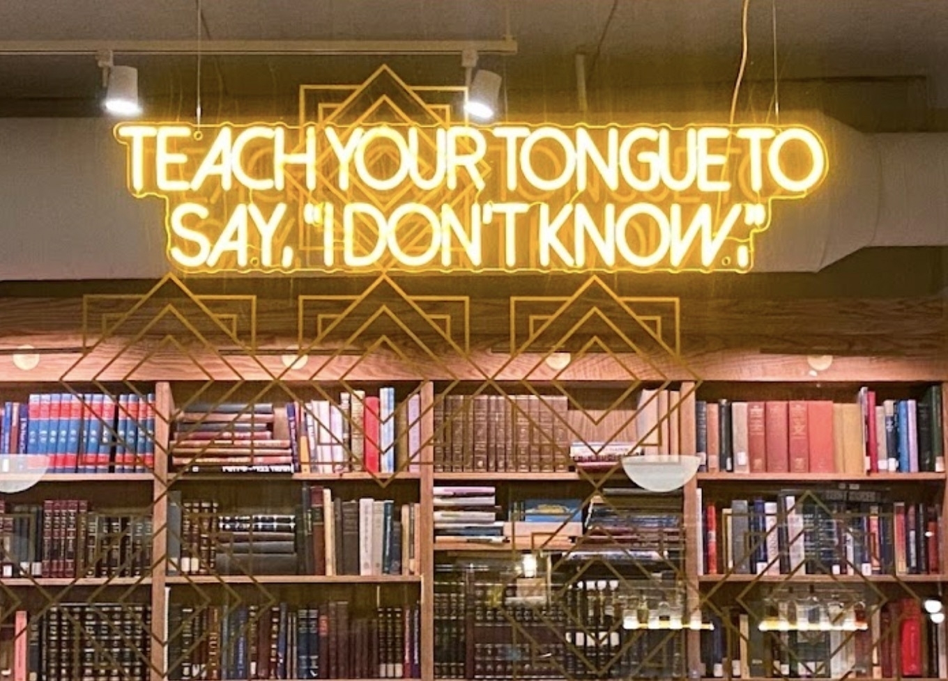 A yellow neon sign that says “Teach your tongue to say “I don’t know”