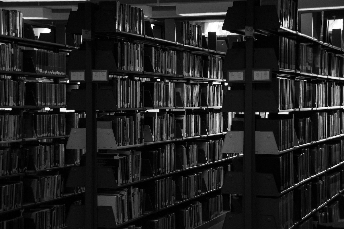 A black and white photograph of library bookshelves in the dark