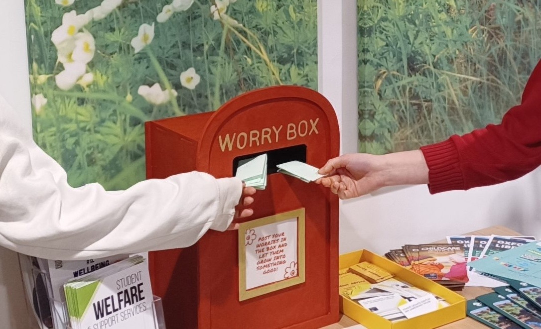 Two arms place folder notes into a small box shaped like a red British postal box, which says "Worry Box" on it