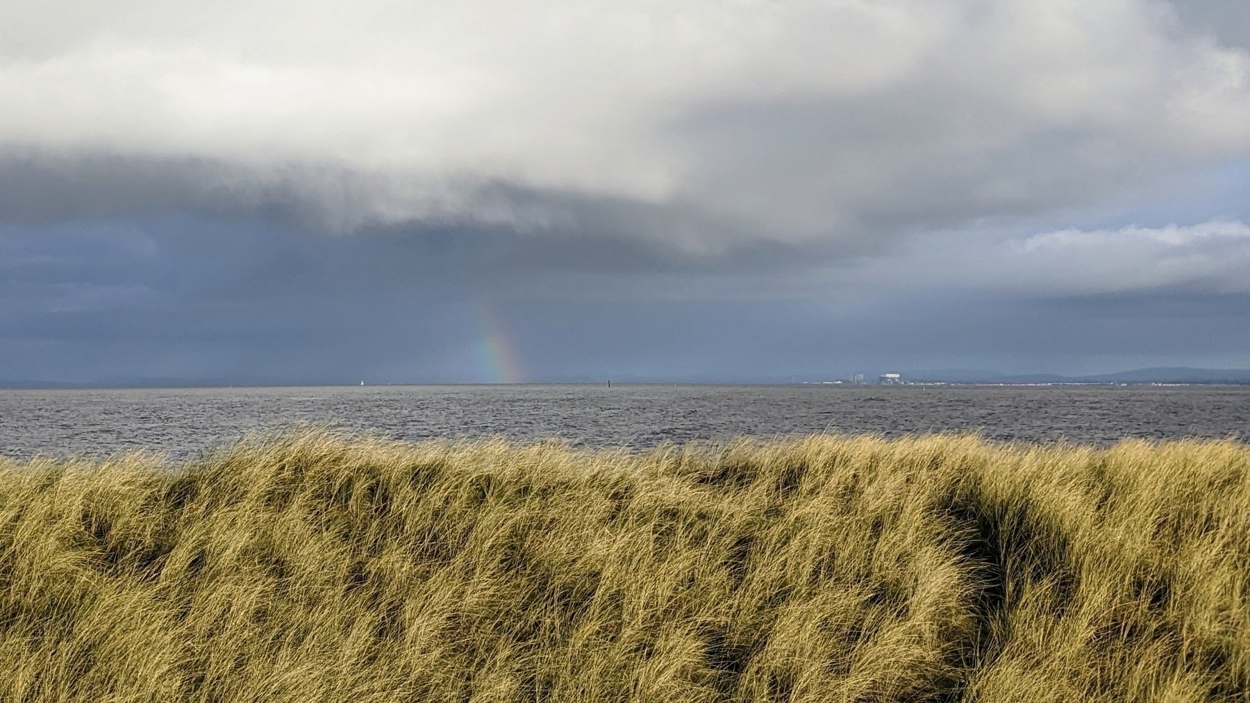 Distant rainbow beginning on the horizon on a moody grey day over an estuary