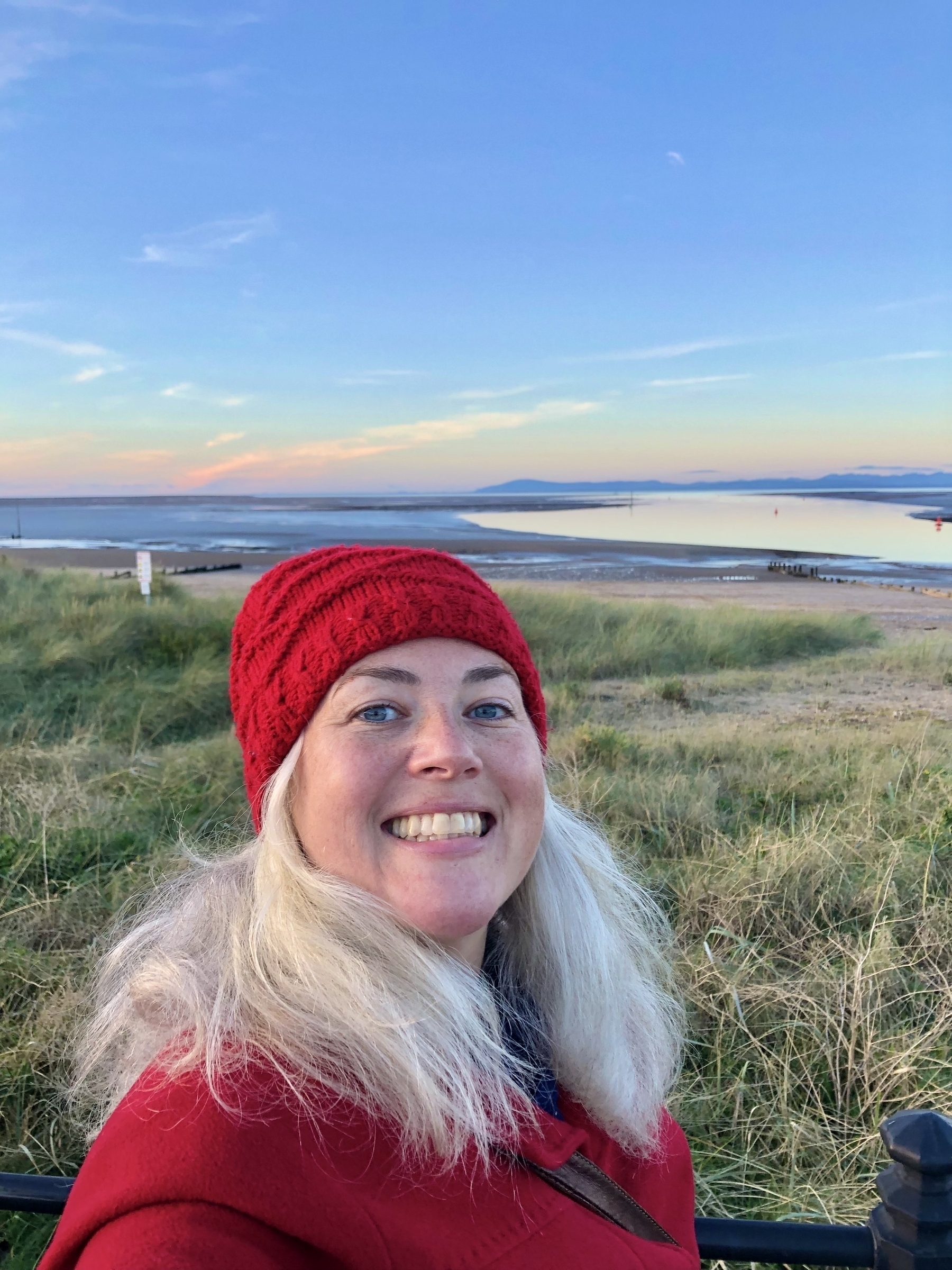 Happy smiling lady in a red hat and long silver hair by the sea