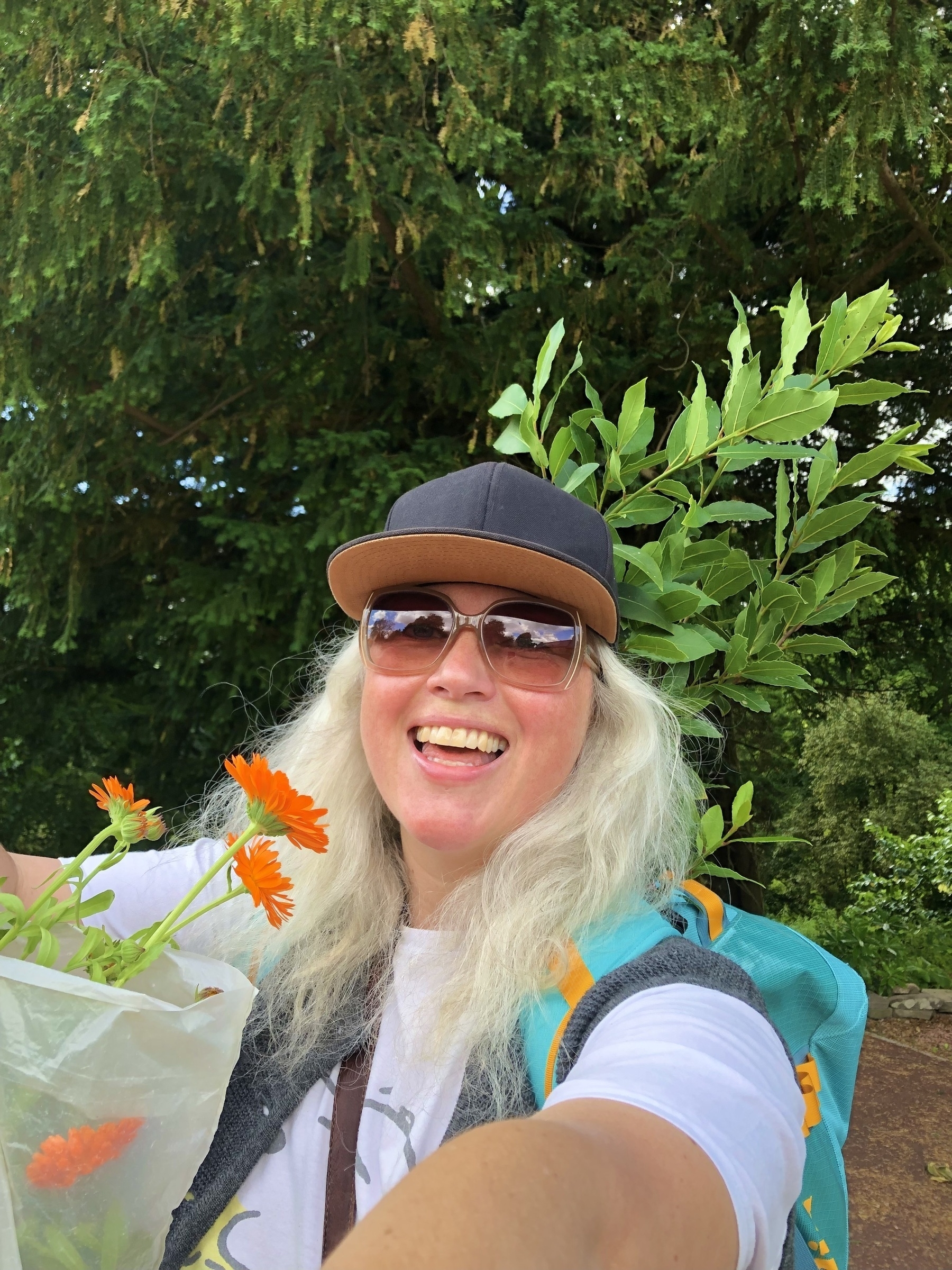 Smiling girl holding orange flowers with a bay tree in her backpack. 