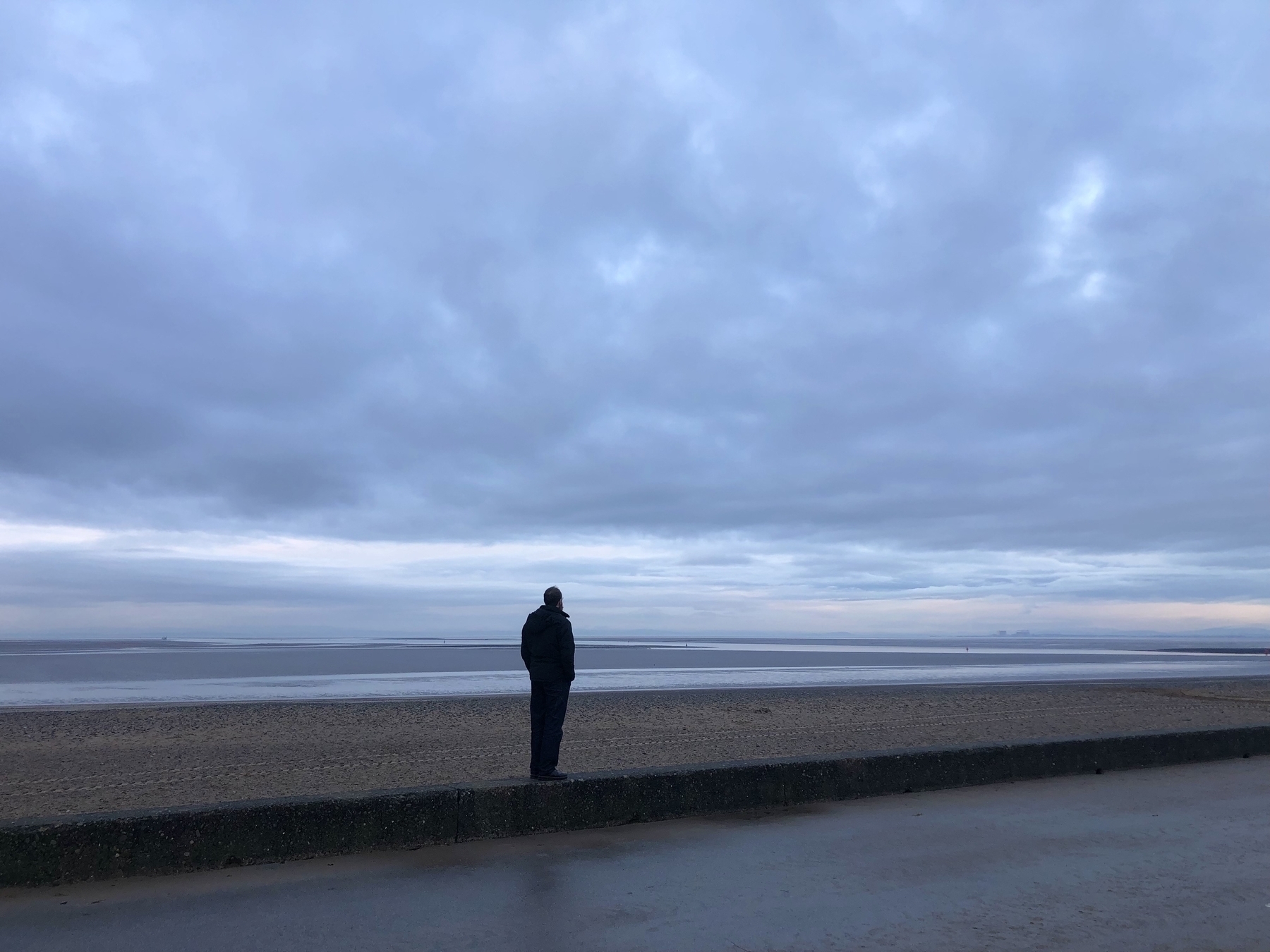 A long shot of the sea with a man standing looking out towards it