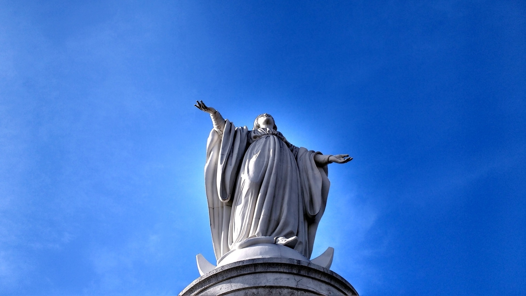 Statue of Virgin Mary with her arms outstretched to a blue sky