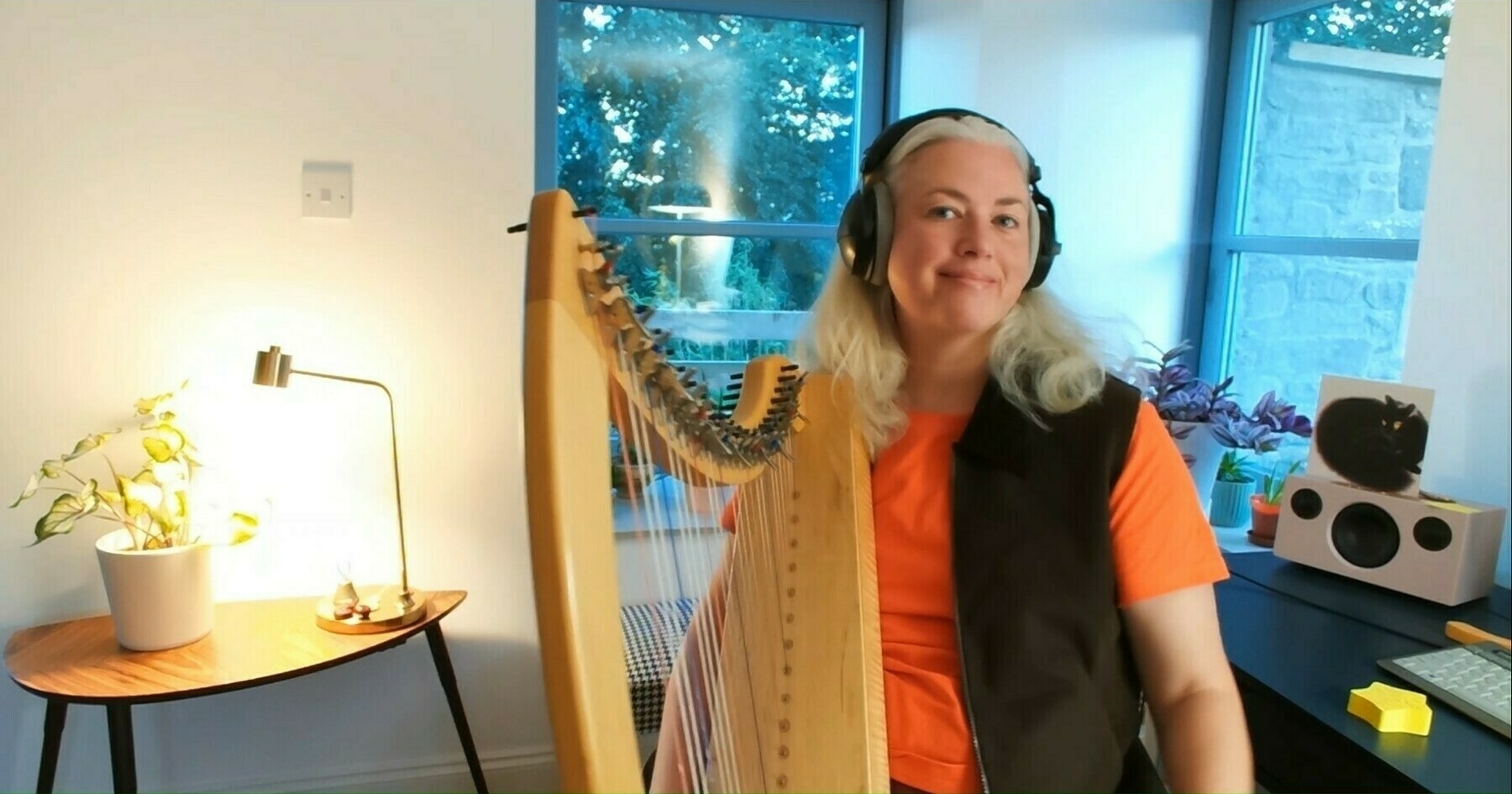 a female, sitting on a chair, looking at the camera in an orange t-shirt holding a harp.