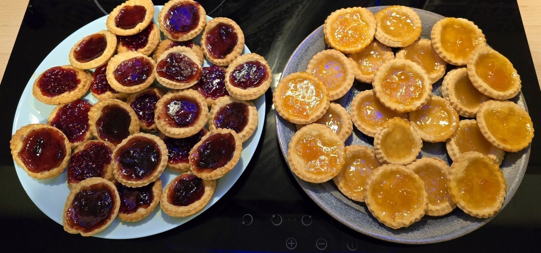 piles of jam tarts in hues of reds and yellows on two blue plates