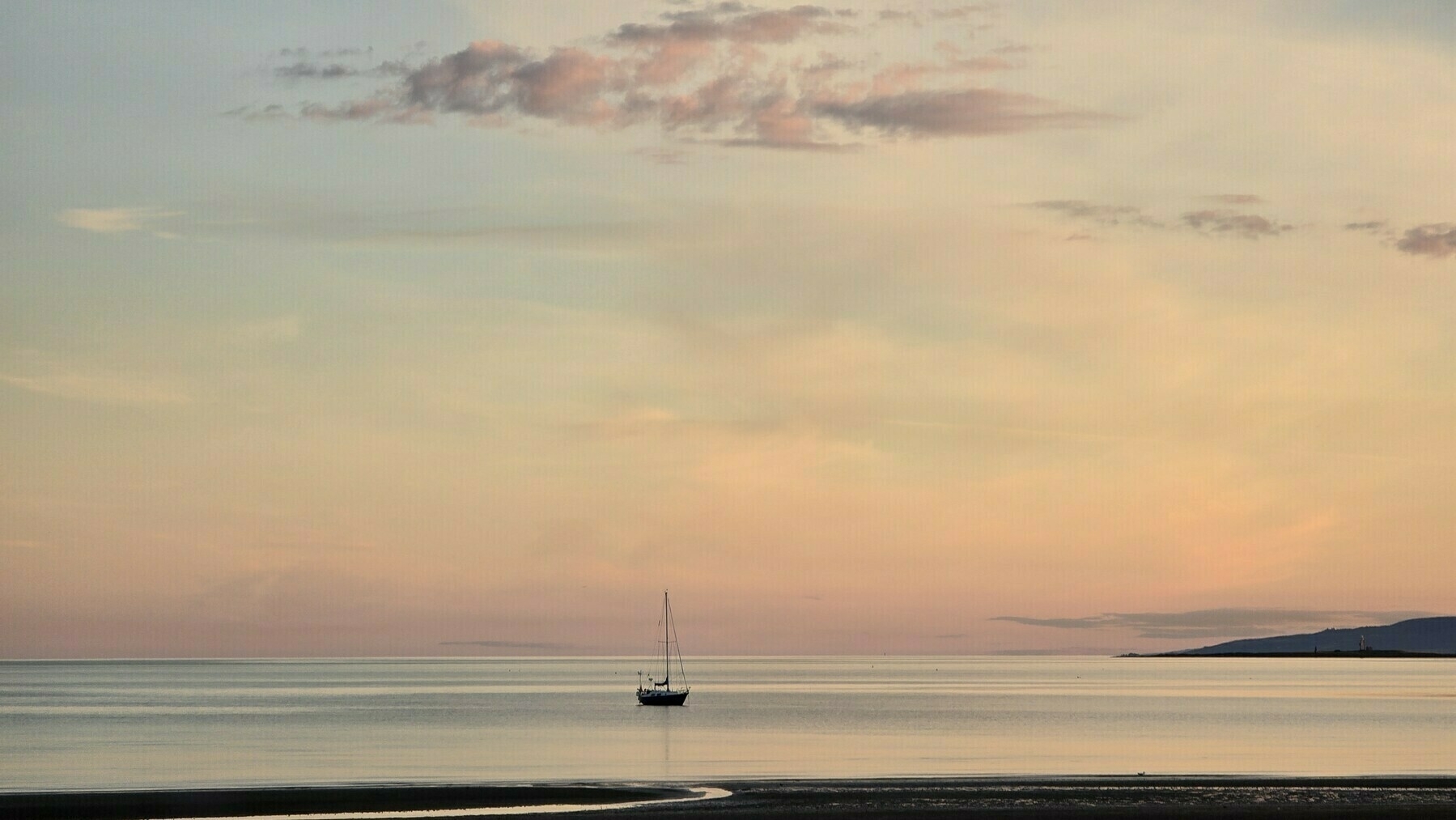 soft pastel sunset of pinks, apricots and blues, a sillhouetted sailing boat rests on a calm sea with the horizon in the background