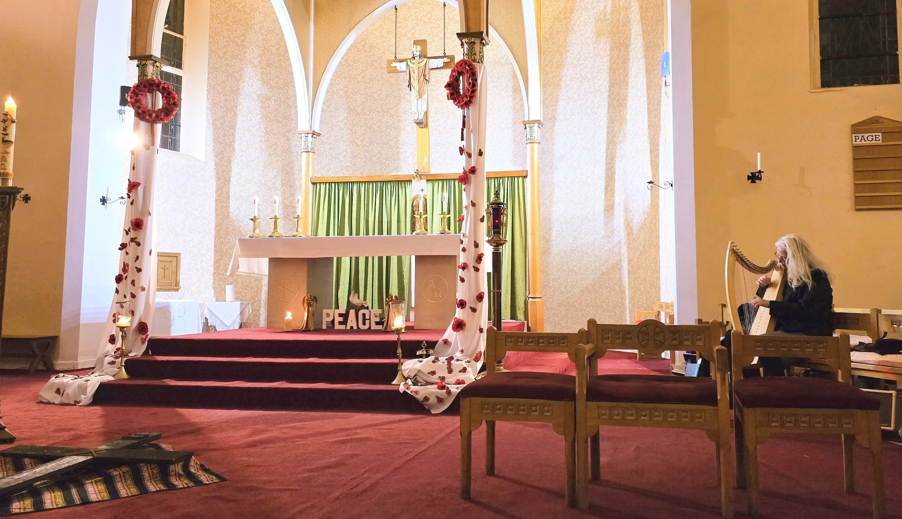 Altar in a church, harpist to the right, red carpet, crucifix in centre, candle to the left. 