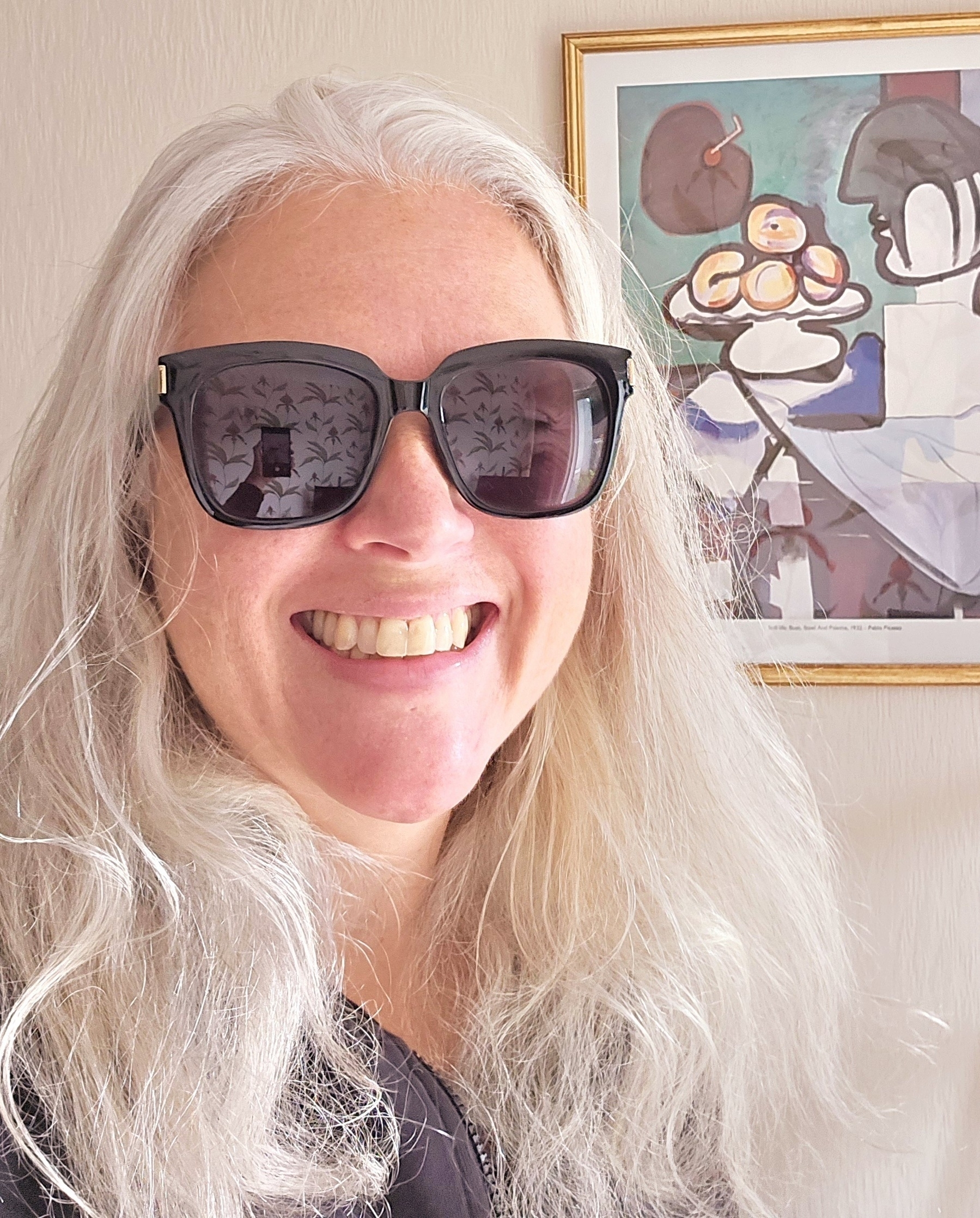 Woman with long silver hair, wearing sunglasses, looking at camera smiling