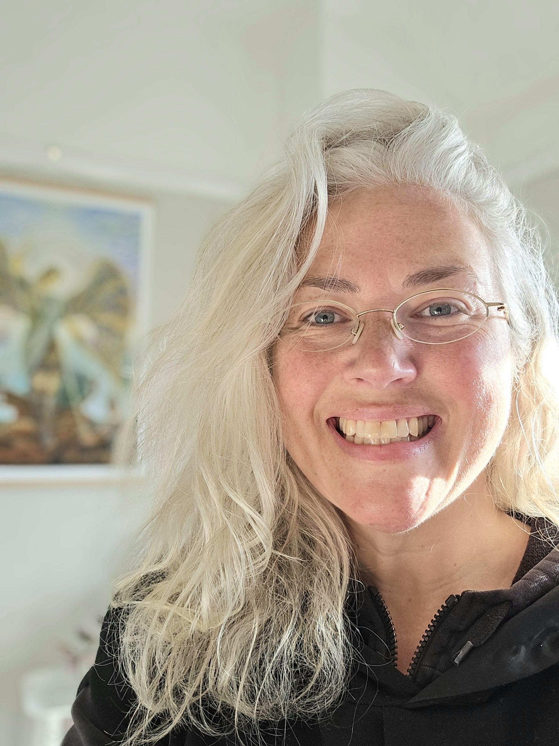 Woman with long, silver hair and gold rimmed specs smiling into the camera