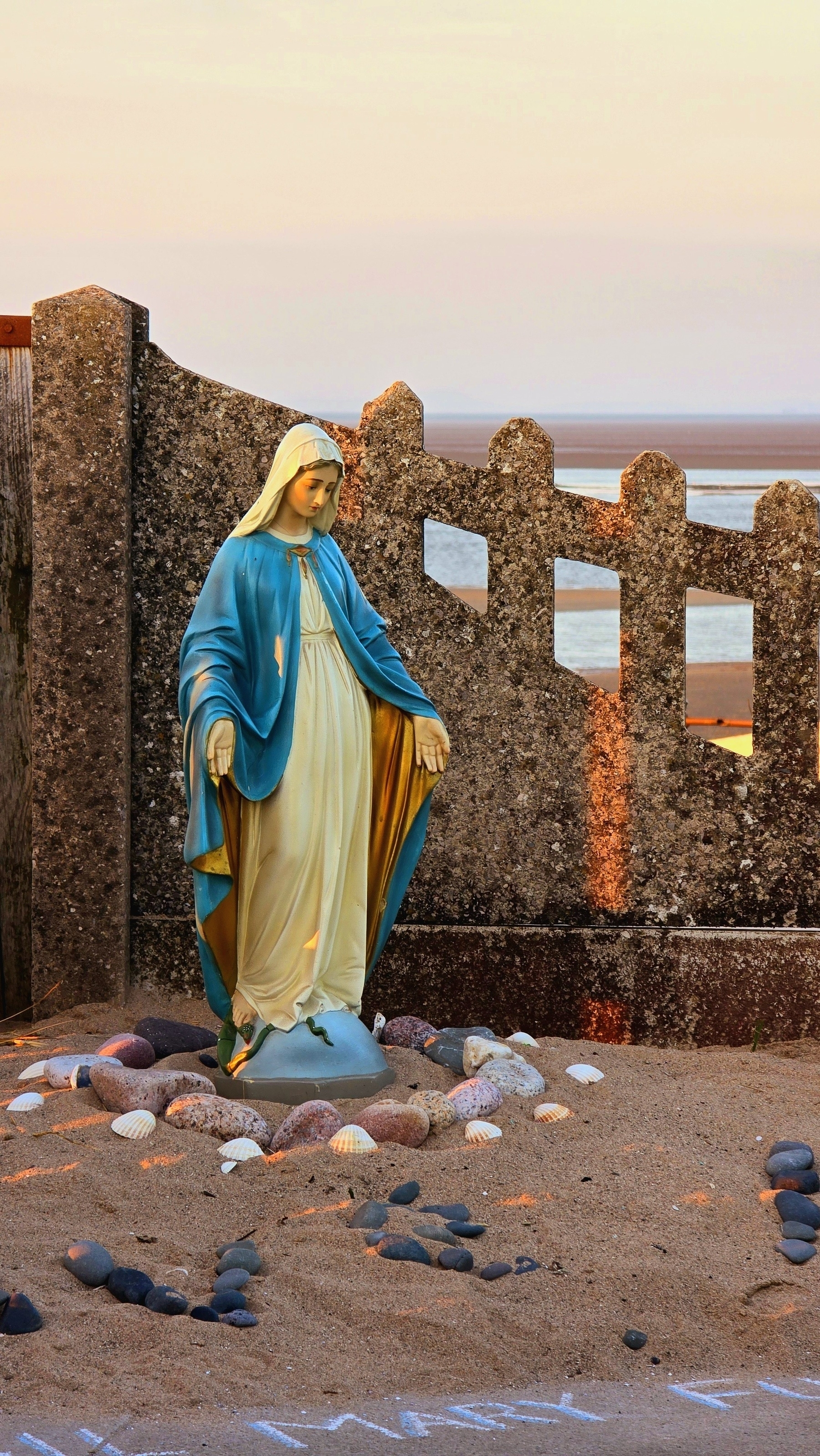 Statue of Virgin May surrounded by pebbles, the sea in the background