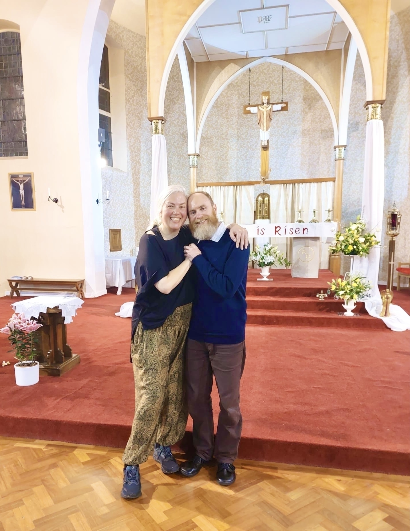 Holly and Simon standing in front of a church altar hugging and smiling