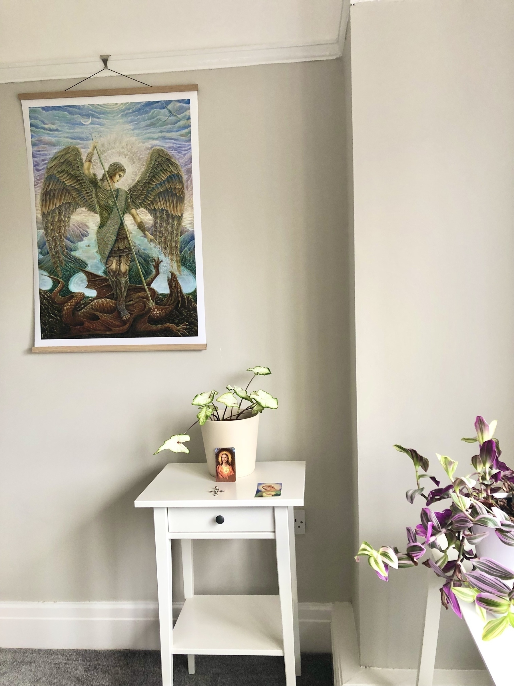 Painting of Saint Michael above a white table with a white plant on it. 