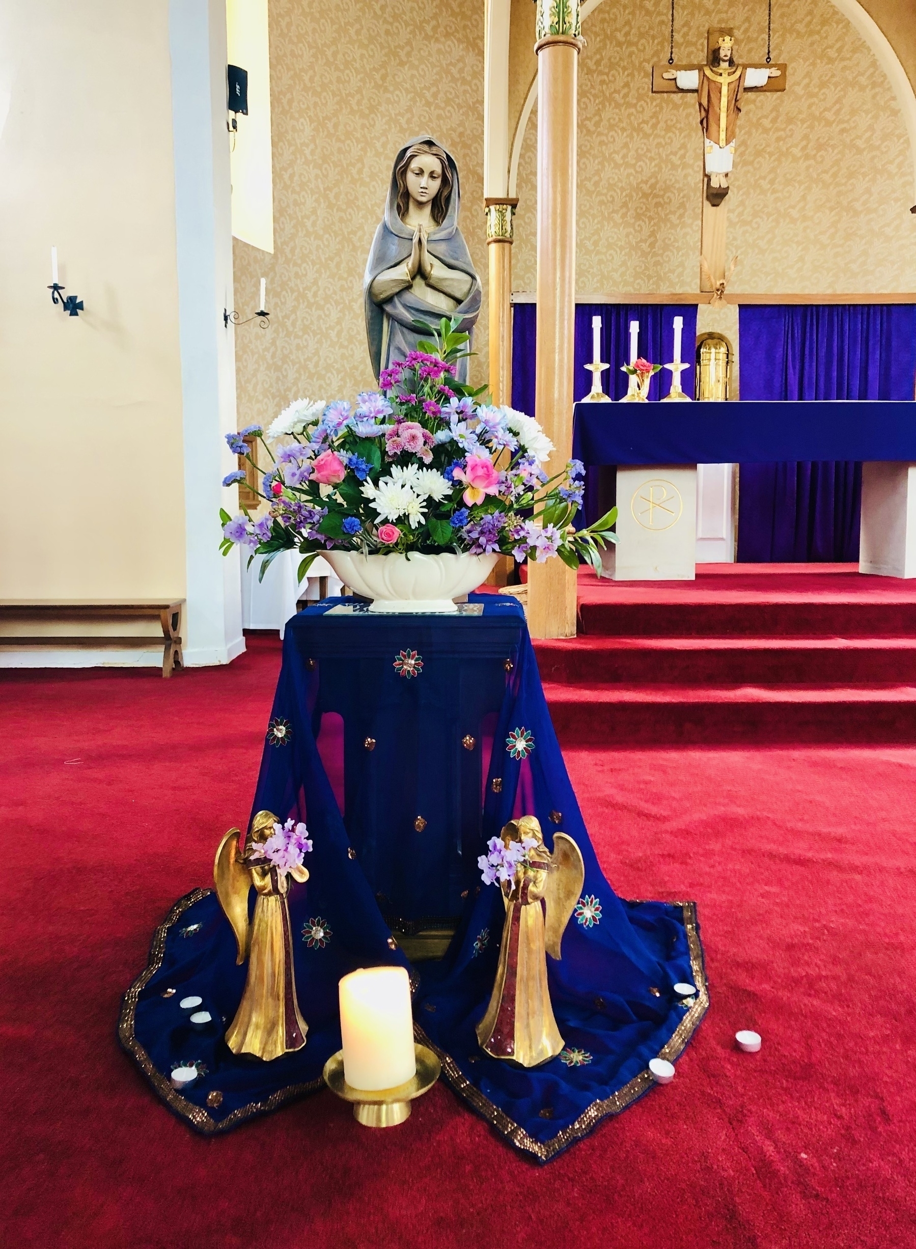 statue of the Virgin Mary surrounded by flowers and angels on a red carpet at the front of church