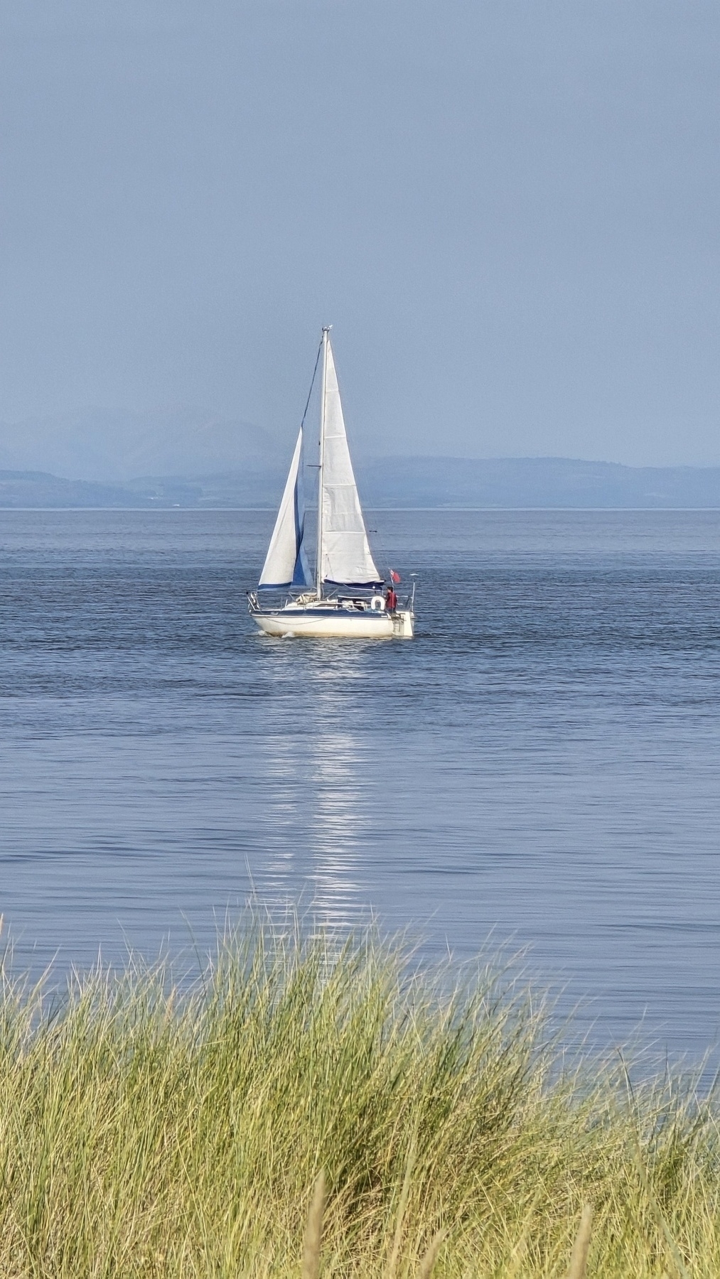 Close up of sailing boat on the sea, the day is bright, the white of the sail reflects on the calm water