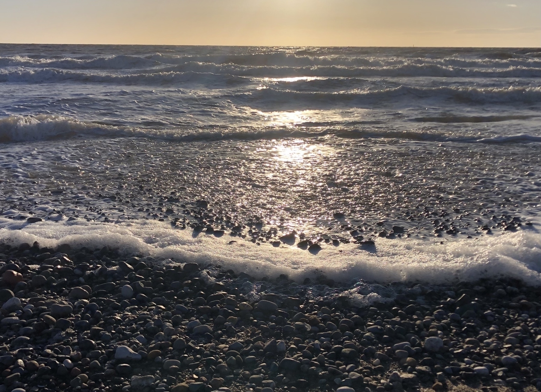 Pebbled seashore and foamy waves in the evening sun