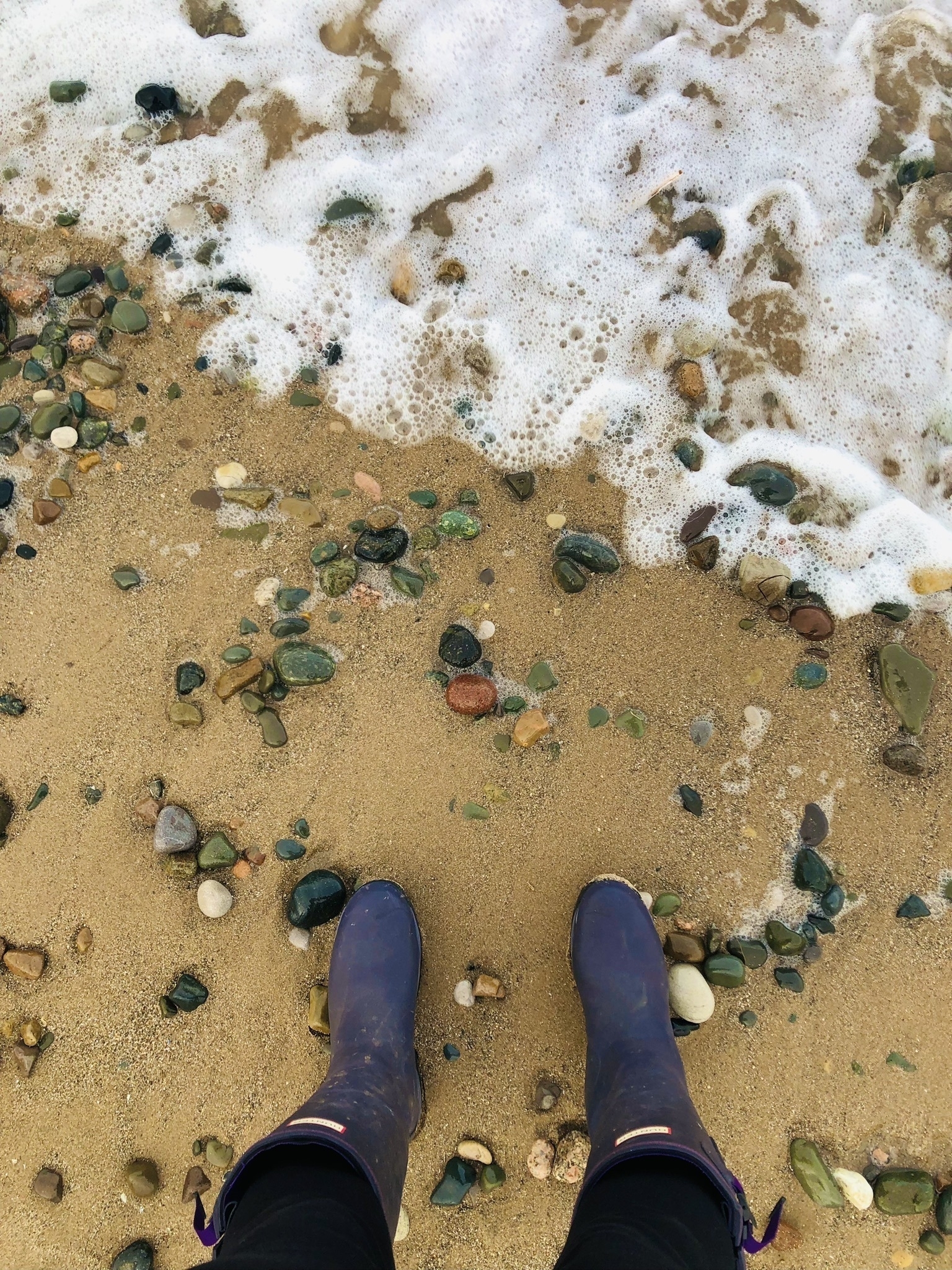 purple wellie boots on a sandy beach with a little sea foam in the corner of the pic