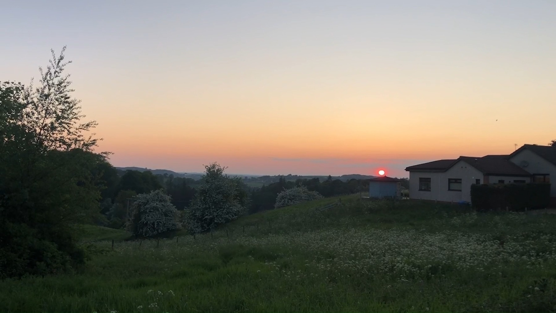 a sunset scene over a green landscape with valley views towards a red, soon to set, sun