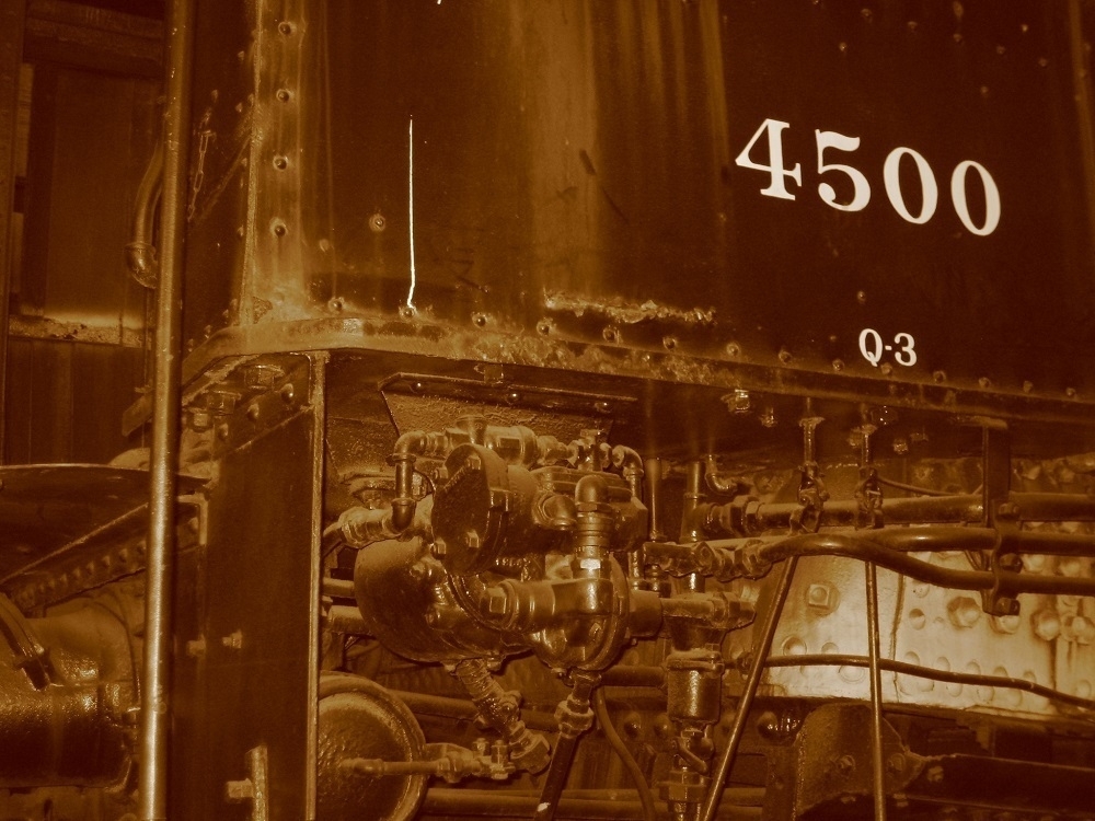Sepia tone. A locomotive cab with the number 4500 displayed on it. Pistons, pipes, and rivets.