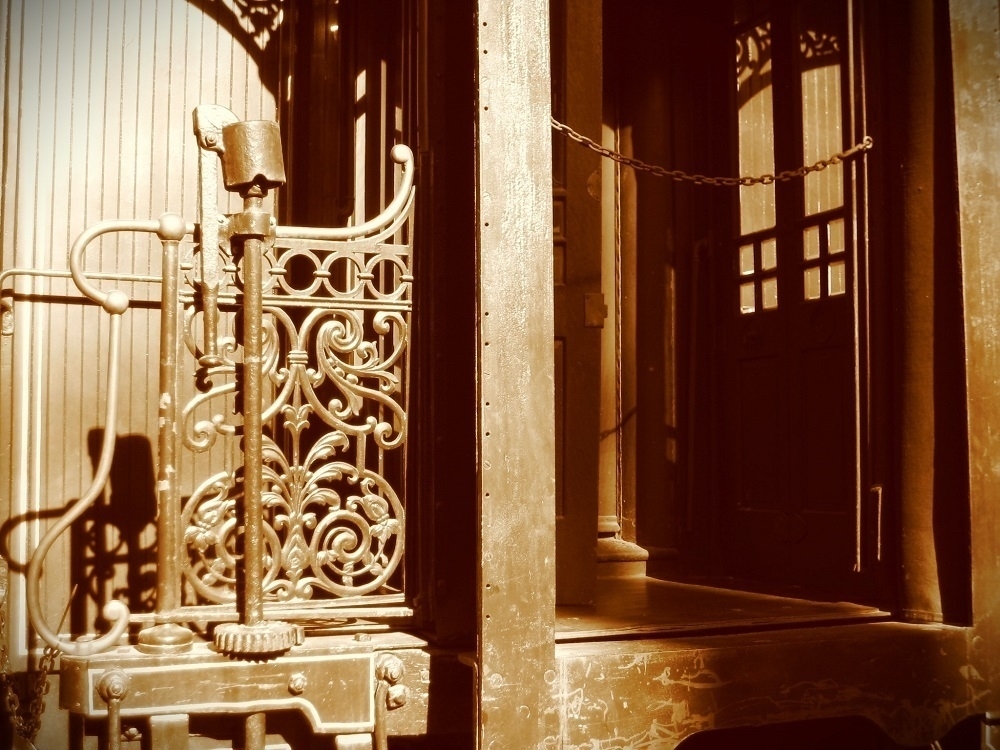 Sepia tone. Wrought-iron entranceway. A window in the background. A single chain guards the way.