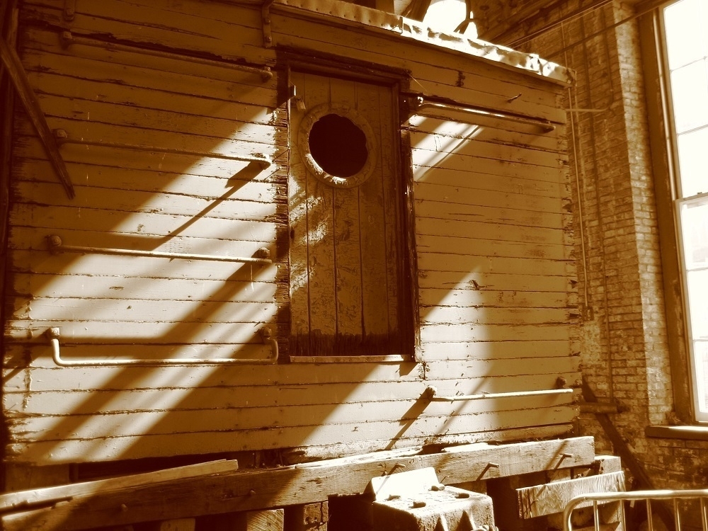 Sepia tone. Back of a wooden train car. A wooden door with a porthole in the center of it.