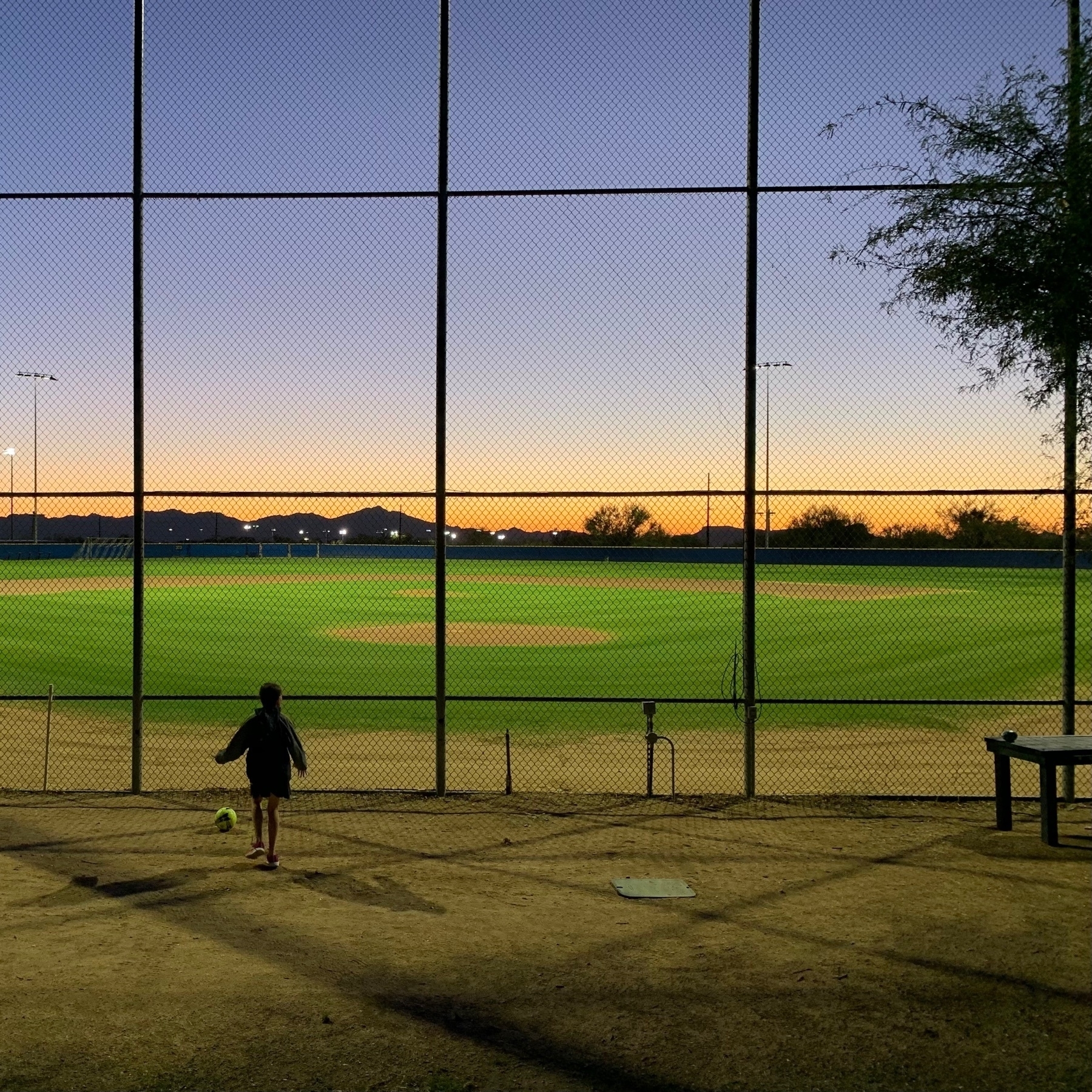 child with ball outside a baseball field at sunset