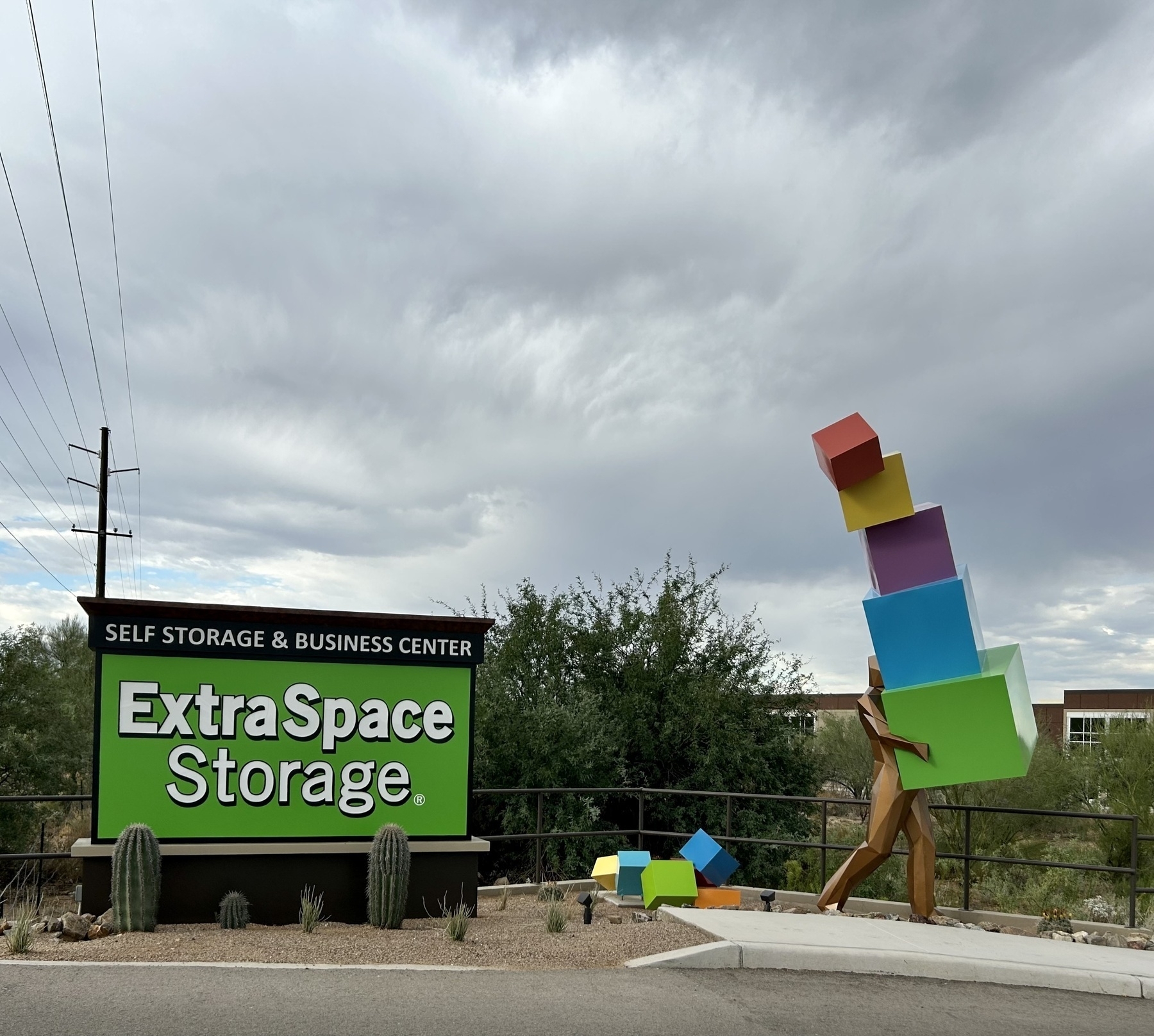 A statue of a man carrying colorful boxes, some of which have fallen on the ground, next to a sign advertising “Extra Space Storage”