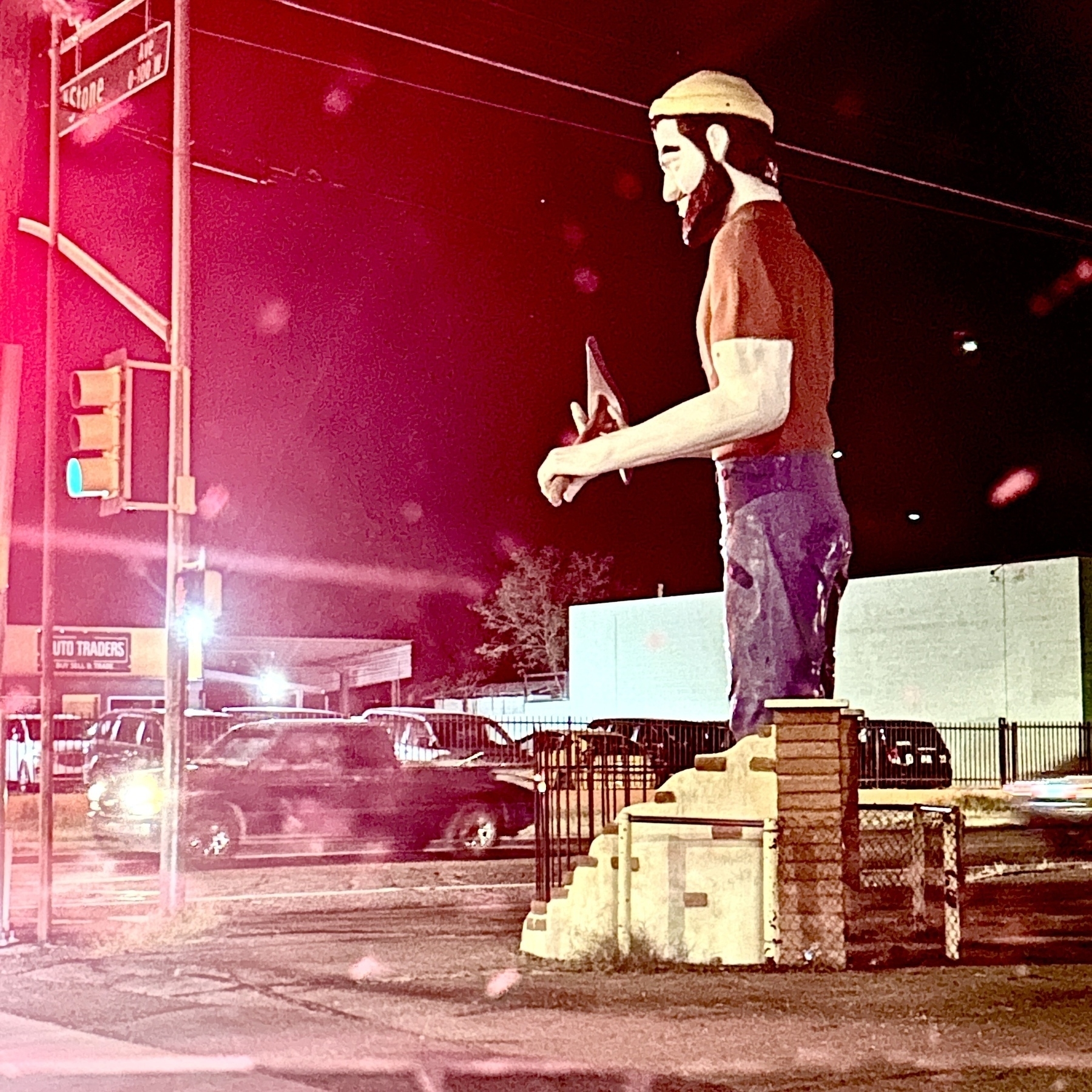 A large statue of a lumberjack holding an axe stands on a street corner at night.