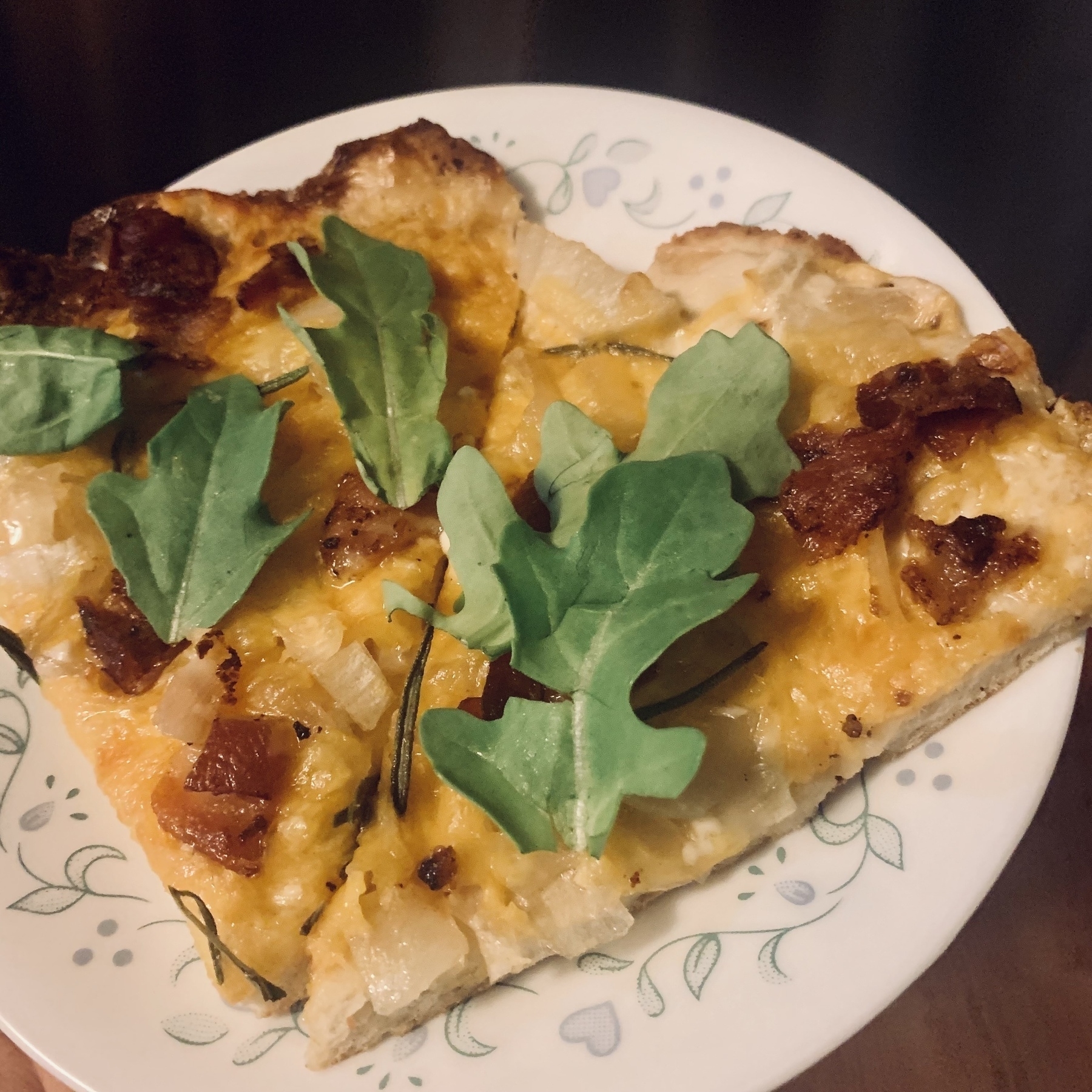 Food on a plate—crisp tortilla with bacon, cheese, and arugula leaves.