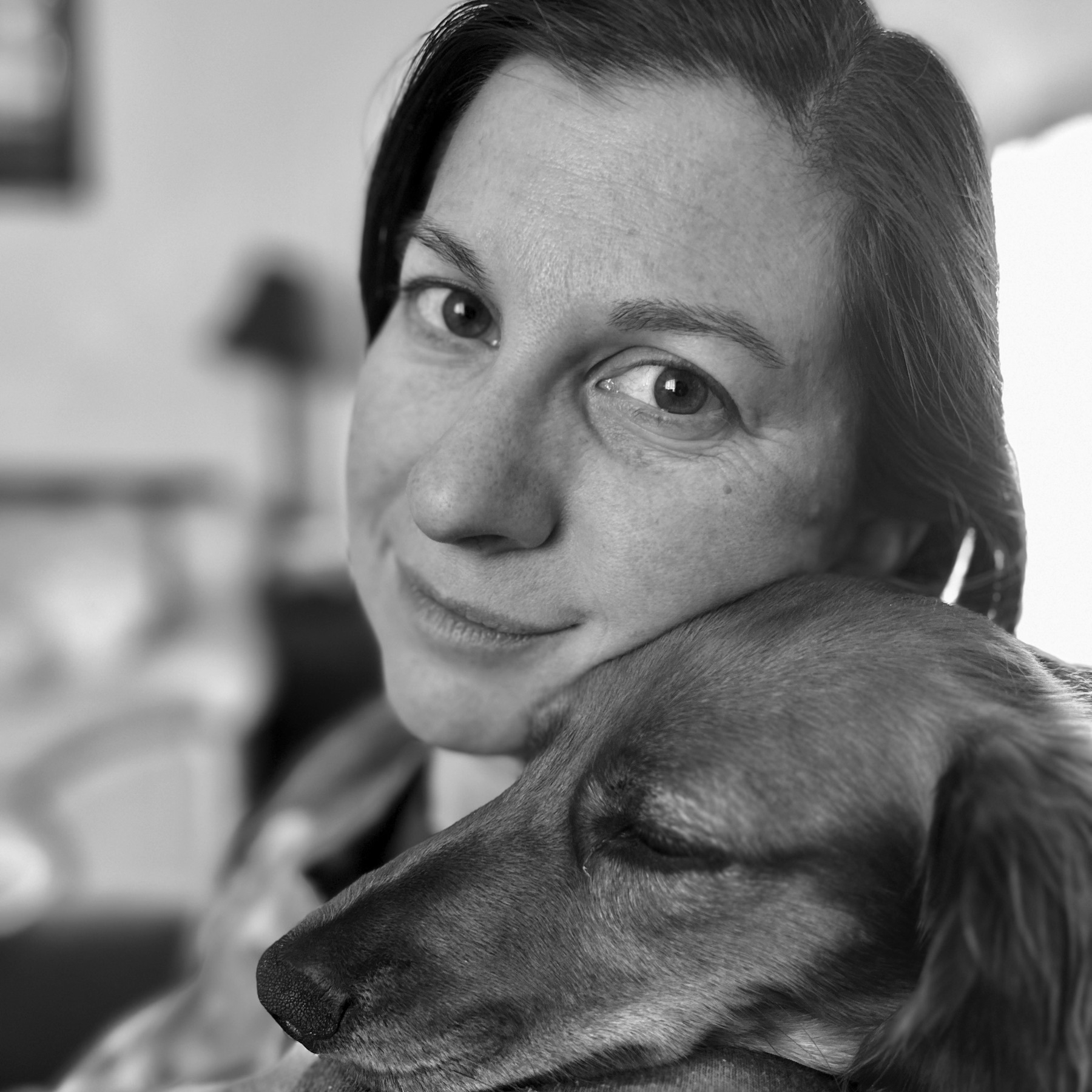 A woman snuggling a dachshund that is laying on her shoulder.