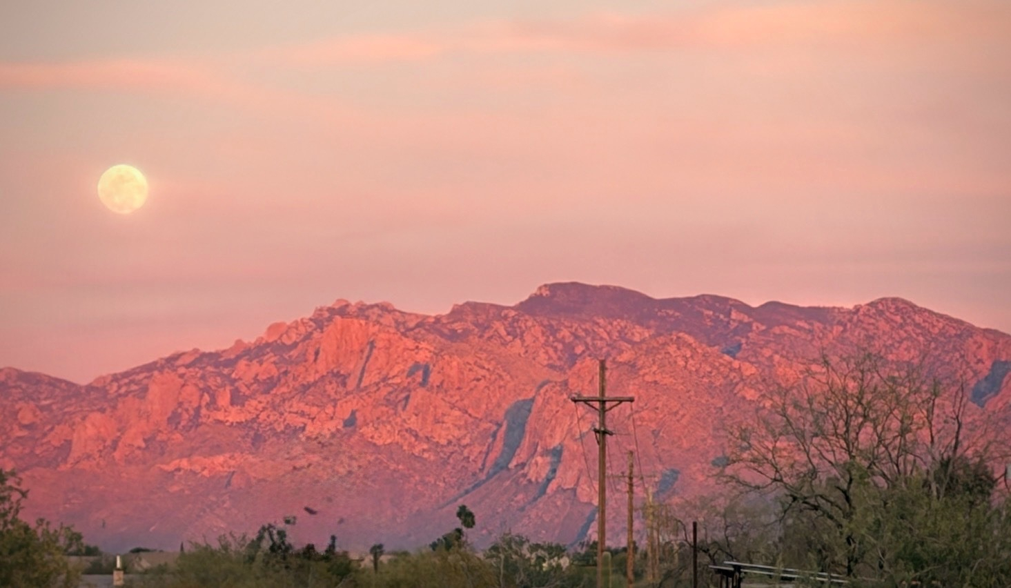The moon rising over the Catalina Mountains in Marana, AZ. The sunset makes the atmosphere an orangey pink.