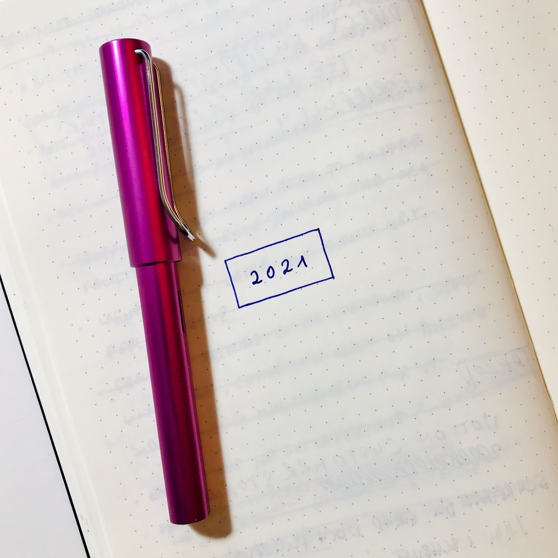 Pink, closed fountain pen laying on a page of a paper notebook. the only thing written on the page is the date 2021 in a box.