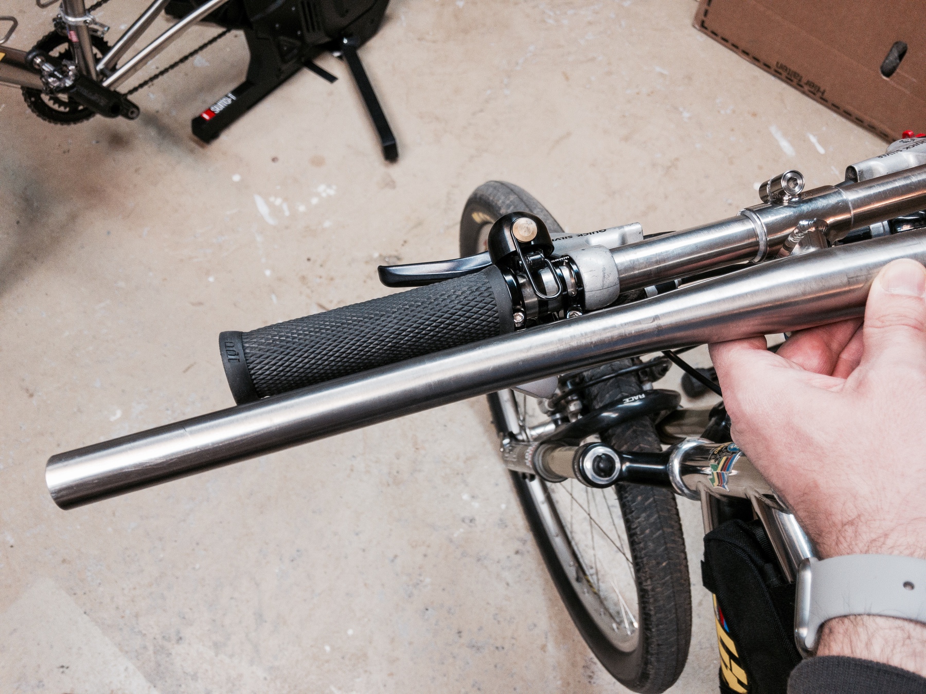 Wide titanium handlebar held over a much narrow handlebar on a bike in a workshop. 