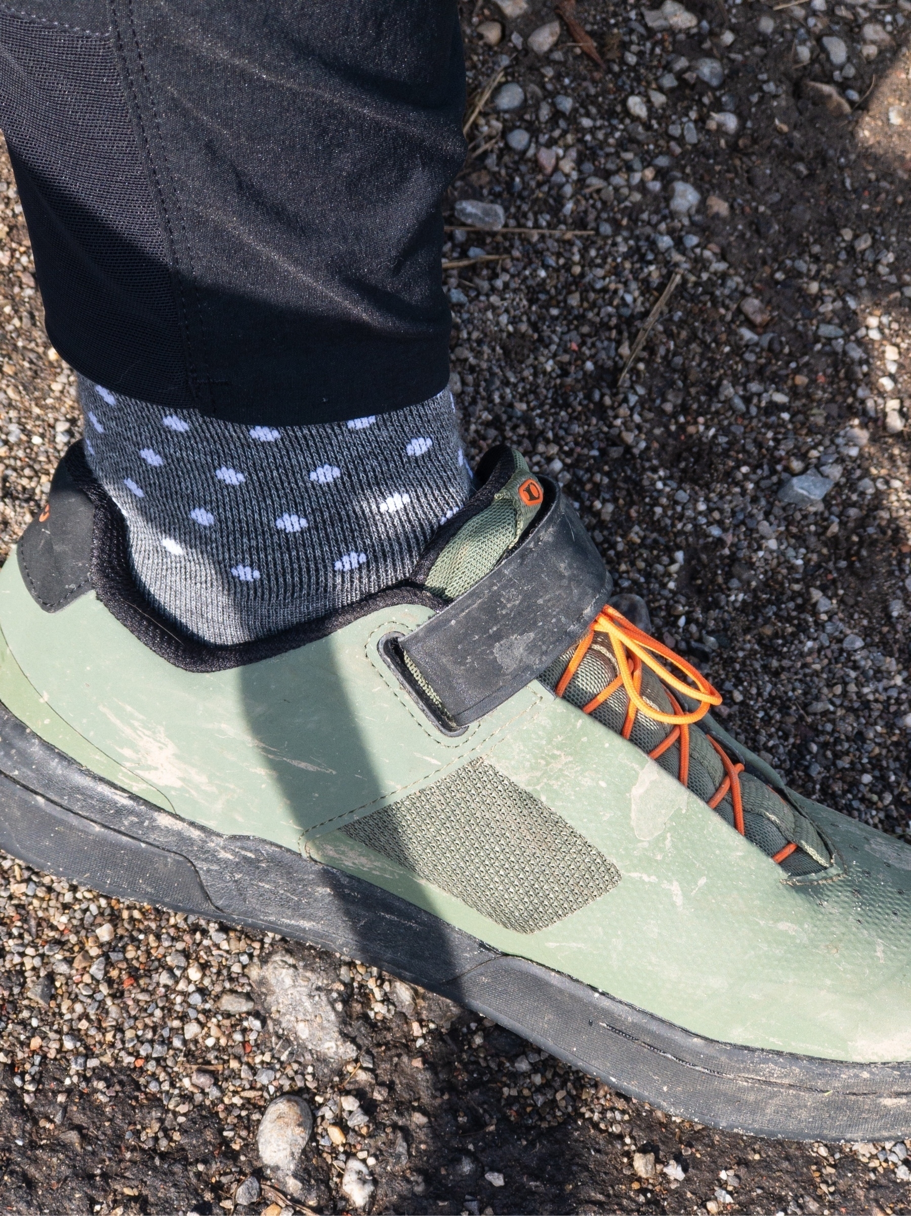 Close-up (from the side) of grey socks with white polka dots in olive green mountain bike shoes. 