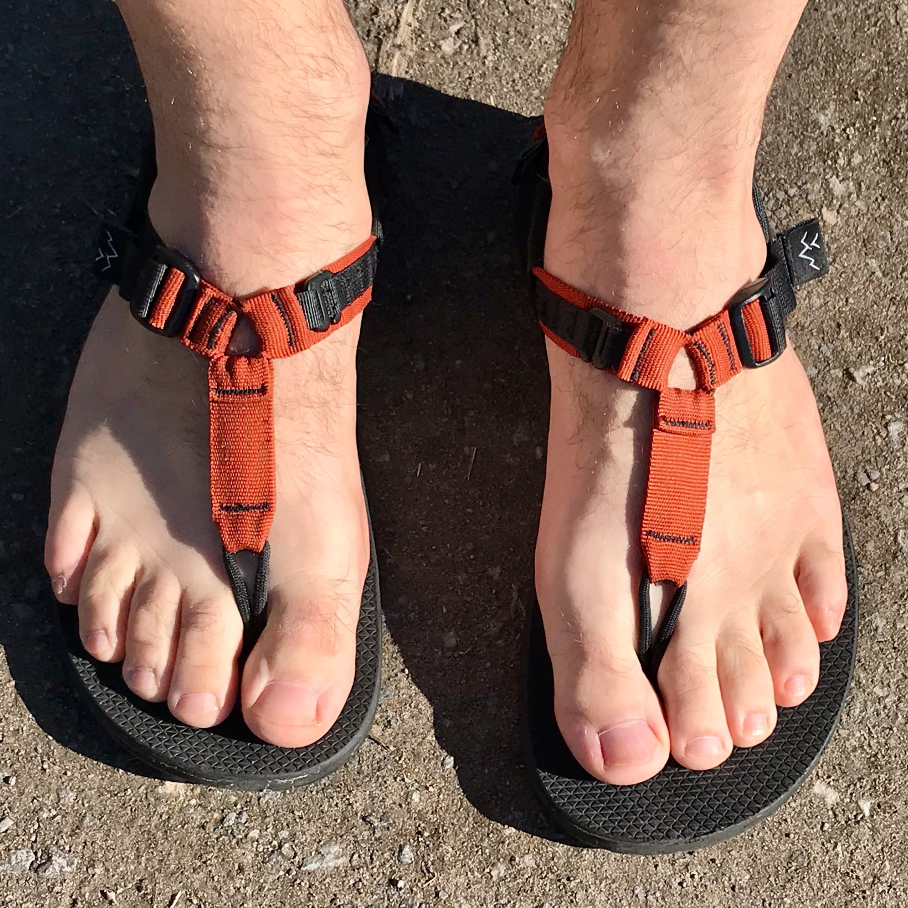 A pair of human, slightly hair feet, very pasty, in sandals with orange straps.