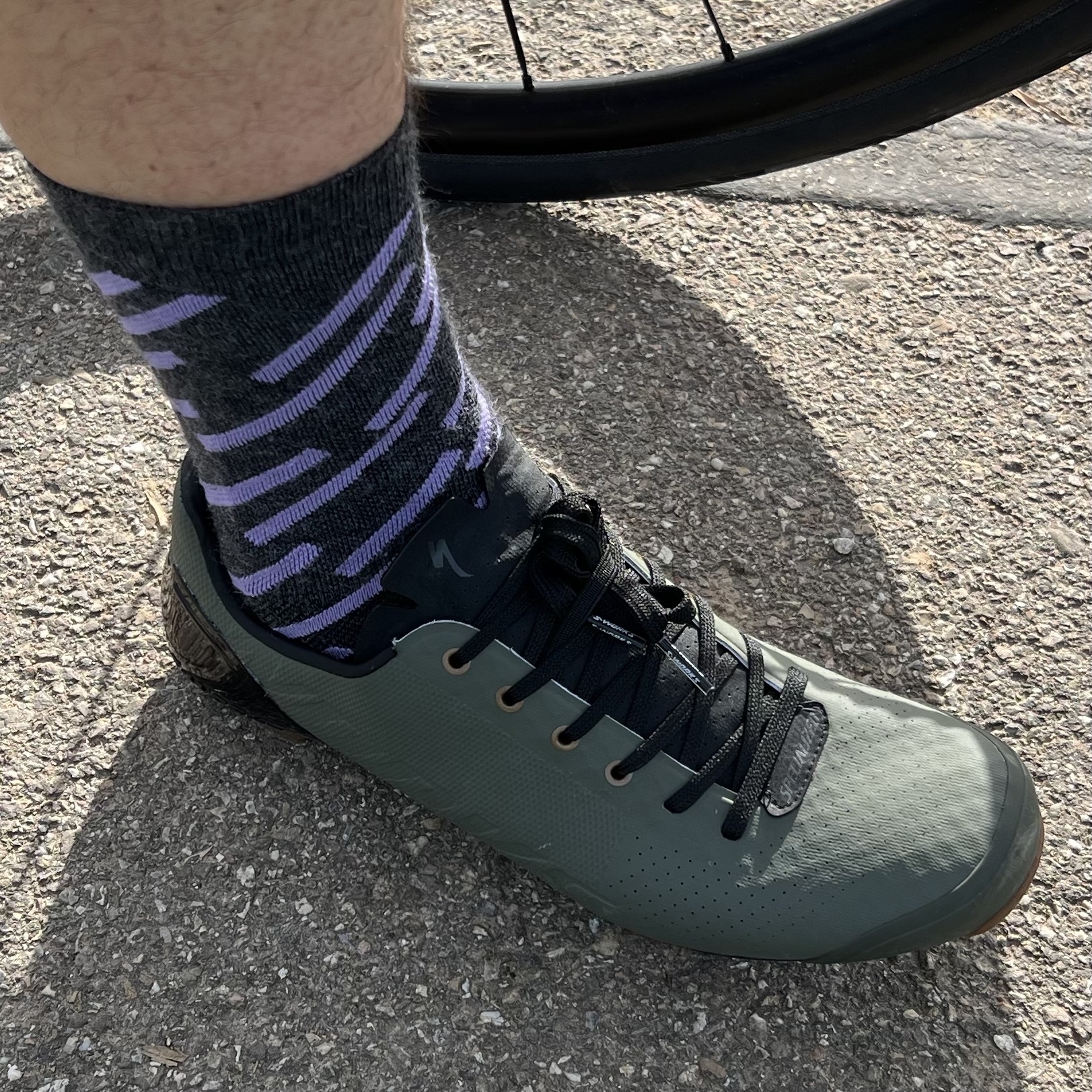 Right foot photographed from the front and left, in a matte teal clipless cycling shoe with black laces. Focus is on the dark grey socks with a pattern of diagonal lavender-coloured stripes.