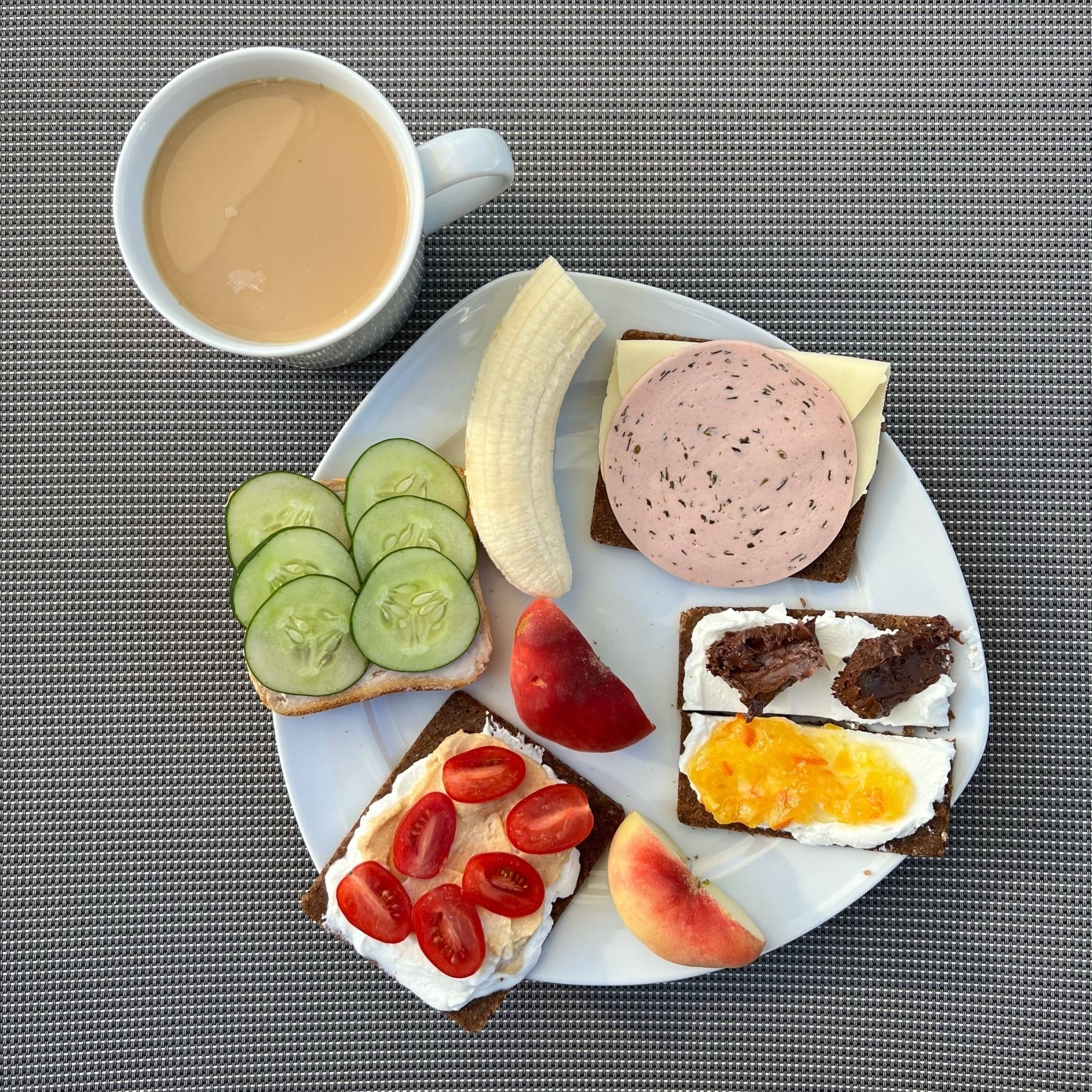 Plate with four pieces of bread with various toppings, half a banana and a doughnut peach, and a mug of coffee.