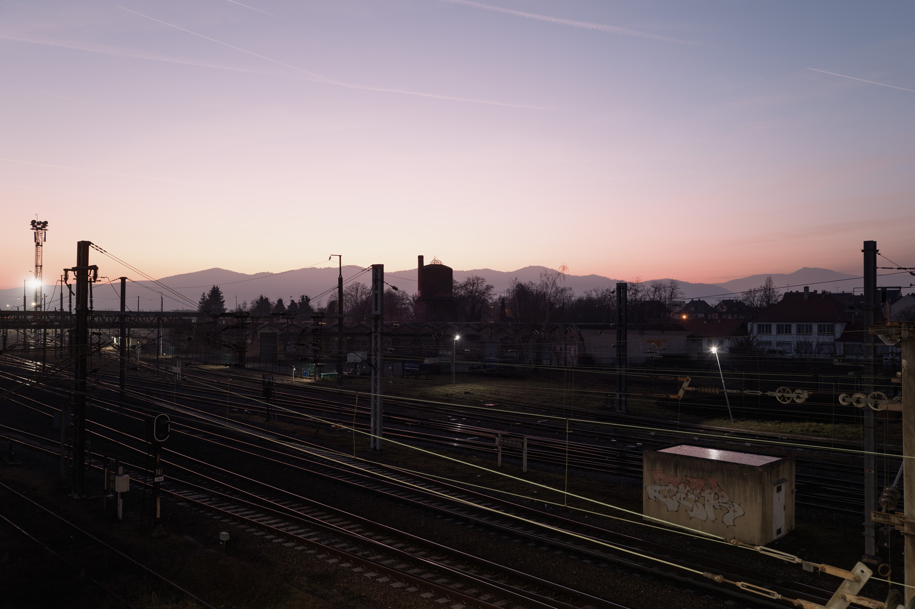 Low light exposure of train station tracks and matching infrastructure captured at dusk. The sky has hues of pink and orange.