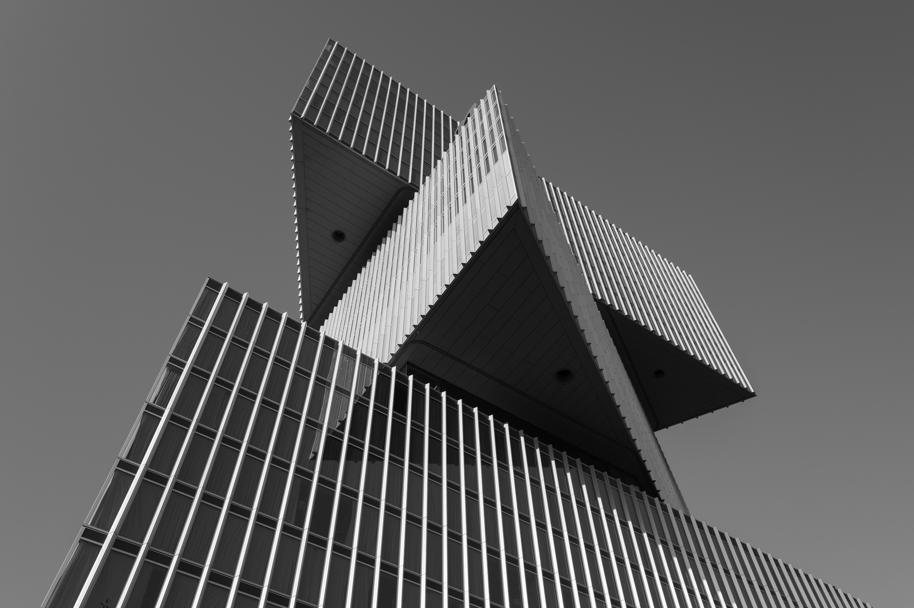 Bottom up black and white shot of the nhow hotel building. It looks like three rectangular bricks with vertical slatting on the outside stacked on top of each other with the tips oriented in different directions.