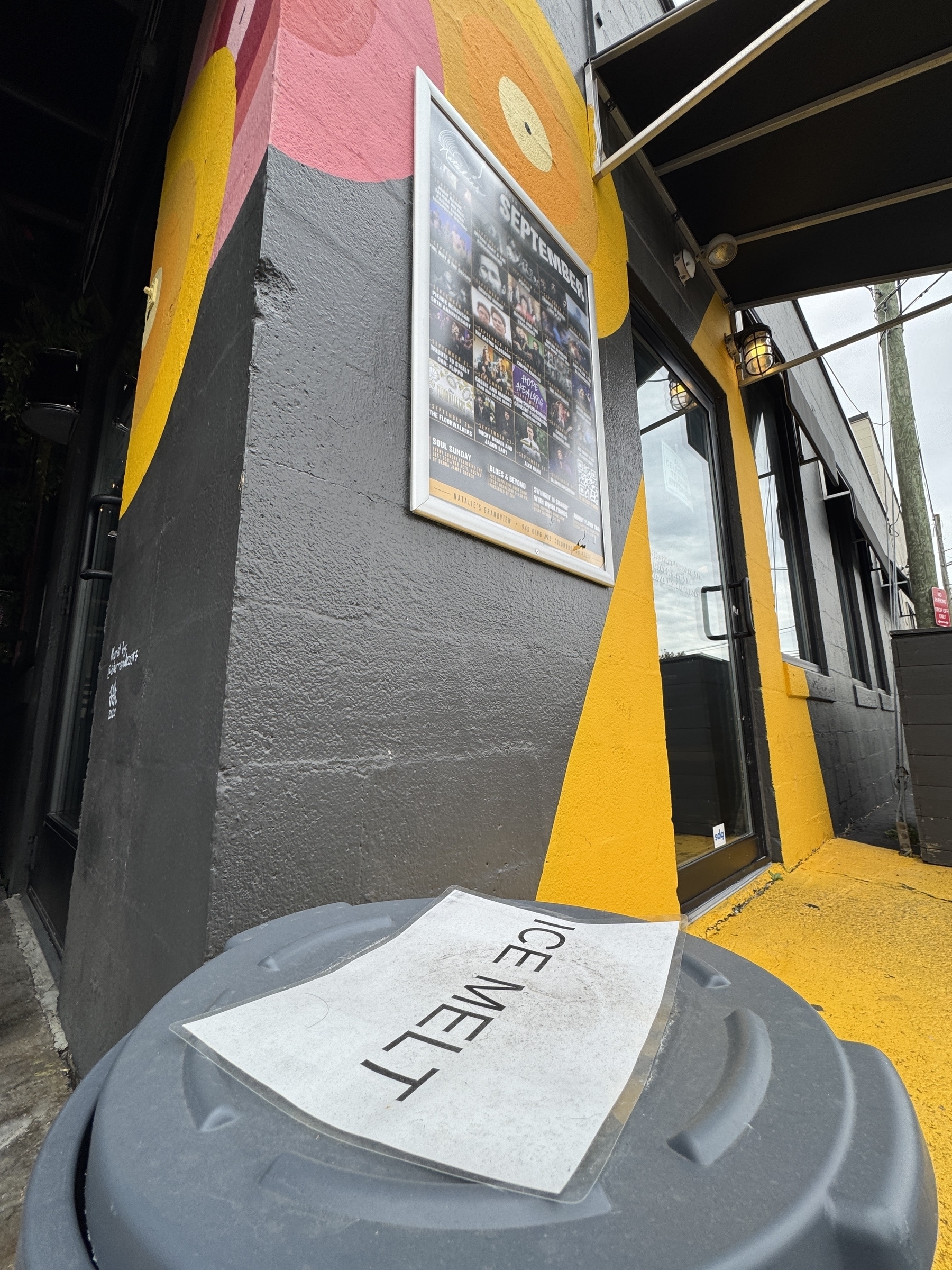 A tub labeled ICE MELT sitting on the ground outside the door of Natalie’s Grandview.