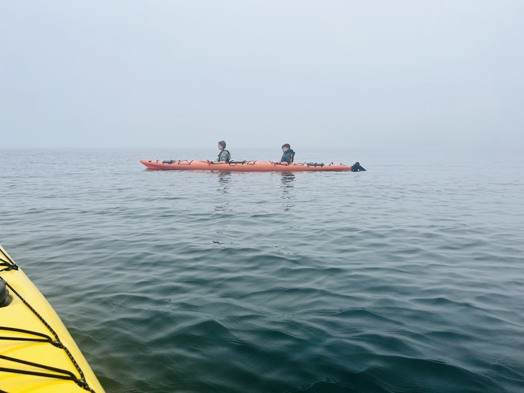 Two teenagers sit in a kayak off the coast of Maine, waiter in every direction 