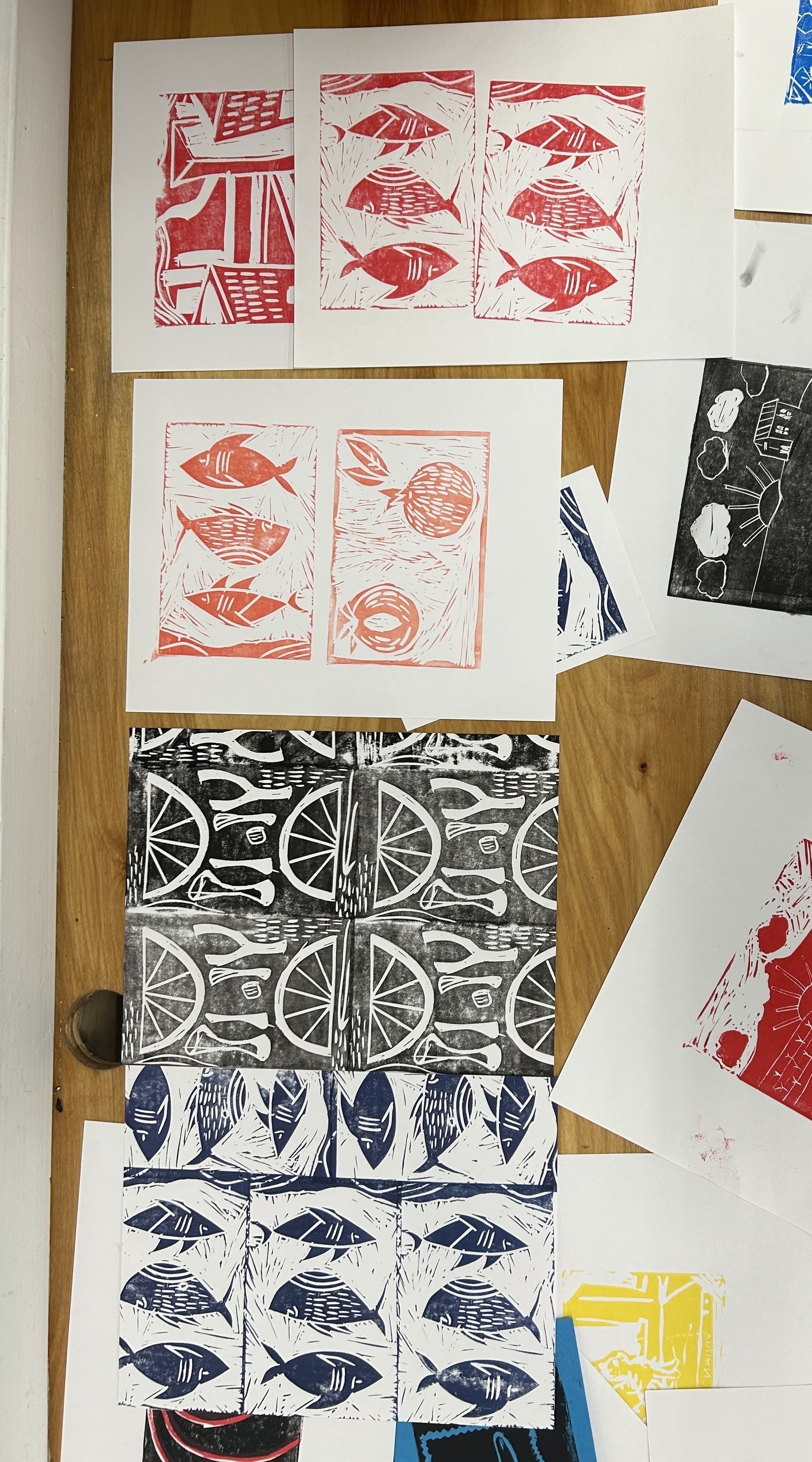 A table is strewn with woodcut prints, some of red or blue fish, some black and white with wishbones and lemon com slices. 