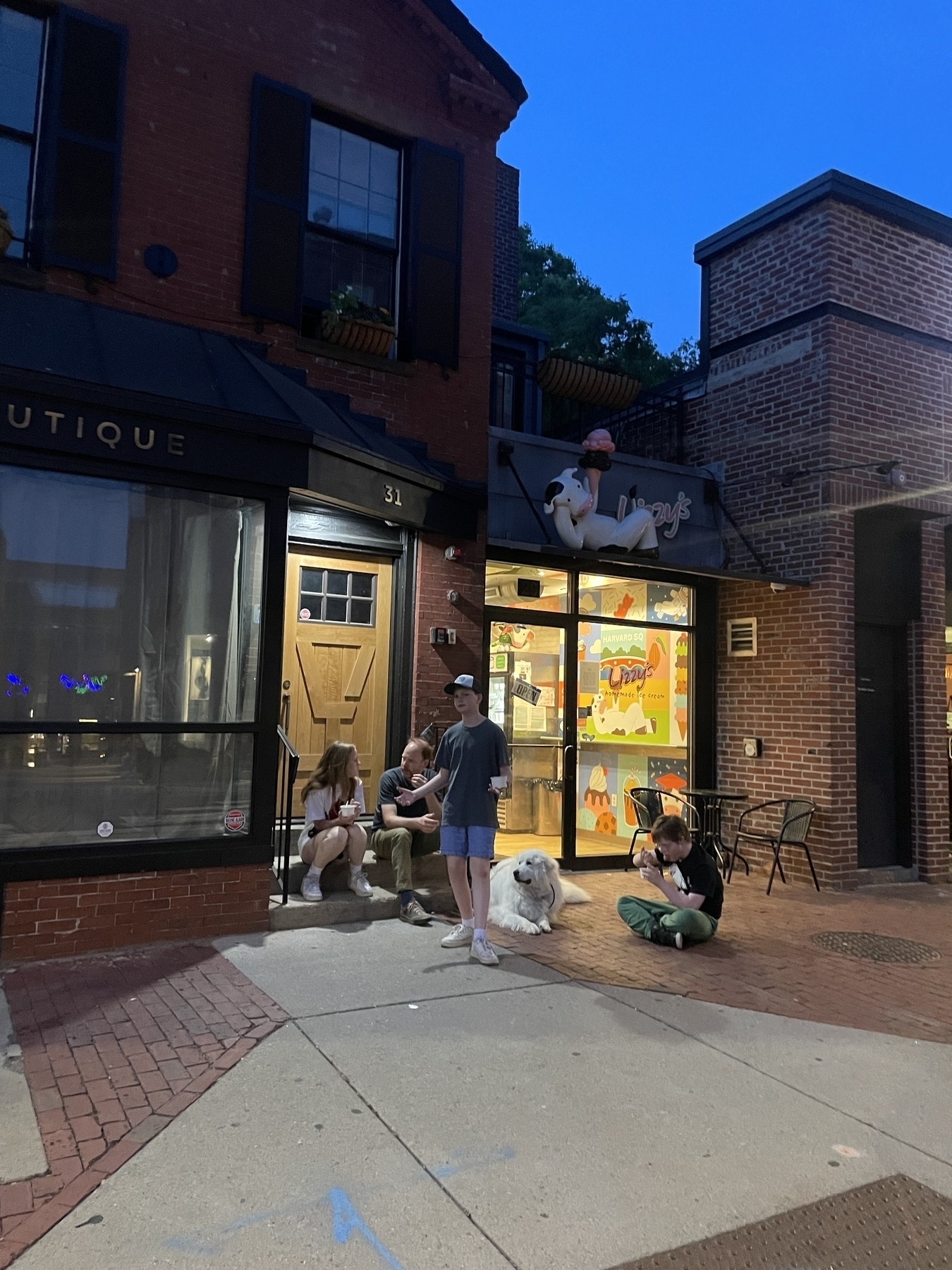 A summer nighttime walk to the local ice cream shop includes my family and our big white dog at leisure, sitting on steps and brick sidewalk.&10;