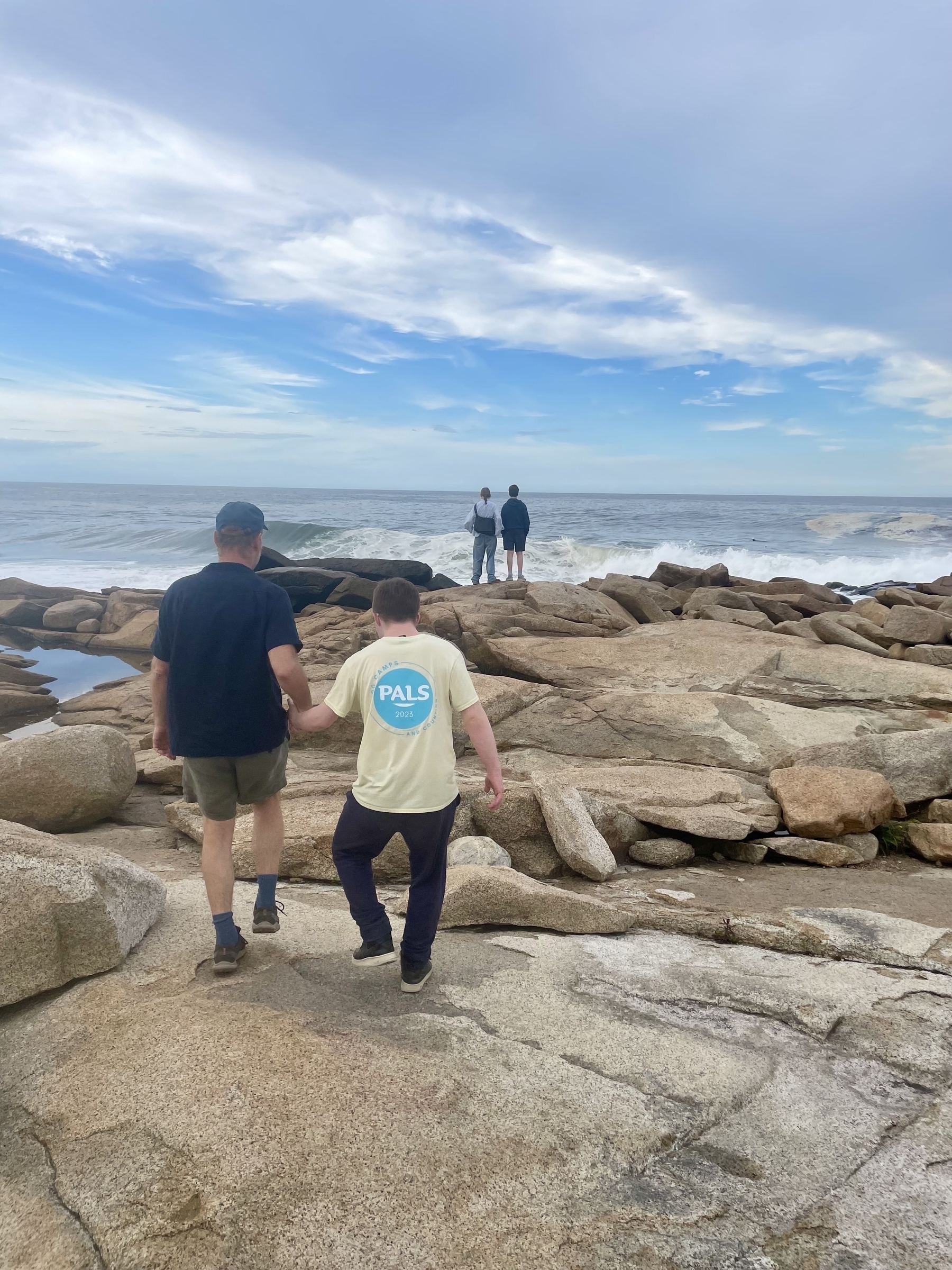 From behind, my family walks the monumental rocks at Halibut Point, ocean stretching out beyond. 