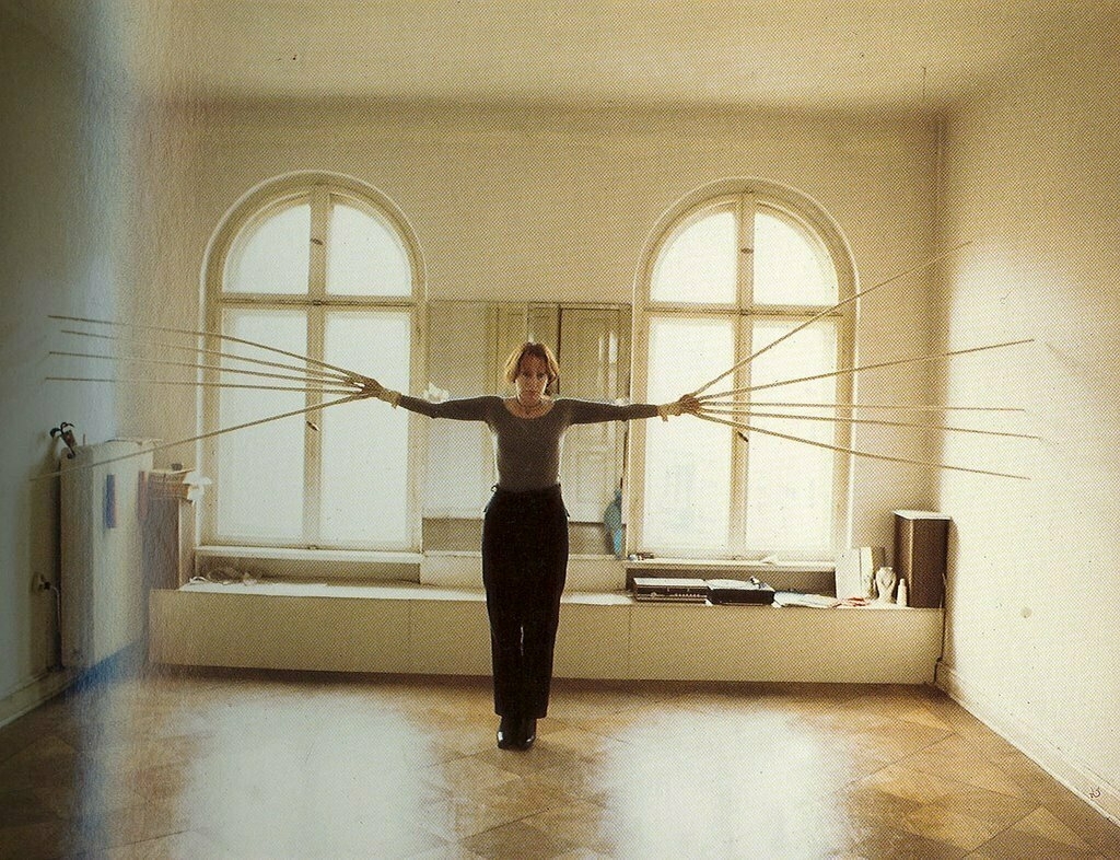 Rebecca Horn in the 1970s stands in a spare studio room with her "finger gloves" of long metal rake-like spikes scraping the walls.