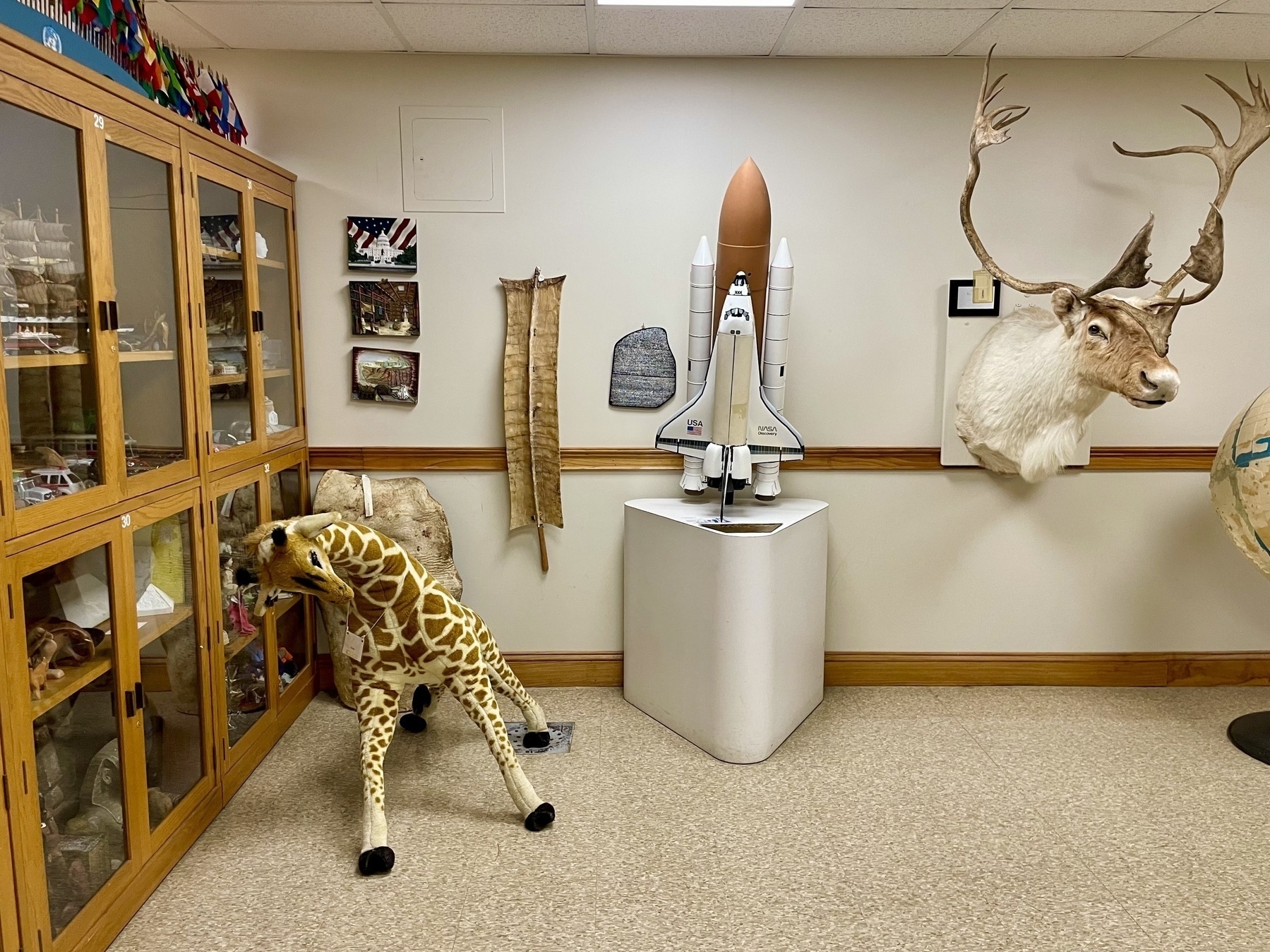 A room in the tactile museum displays a large NASA rocket ship, a taxidermied elk head, a stuffed giraffe, a snakeskin, flags, and other touchable objects.